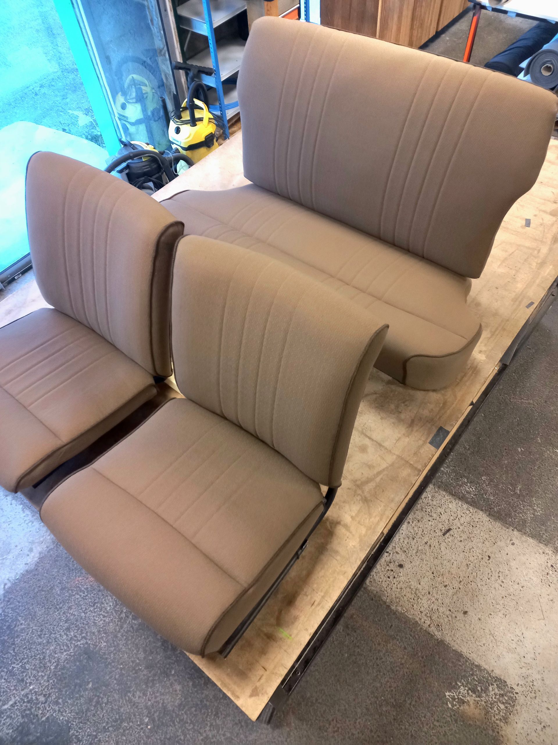 Trois sièges auto beiges rembourrés sur une palette en bois dans un atelier