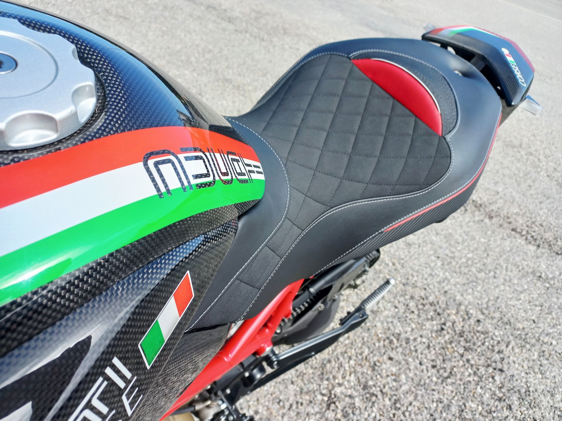 Gros plan sur une selle et un réservoir de moto de sport noirs, rouges et verts, ornés d'autocollants, sur de l'asphalte.