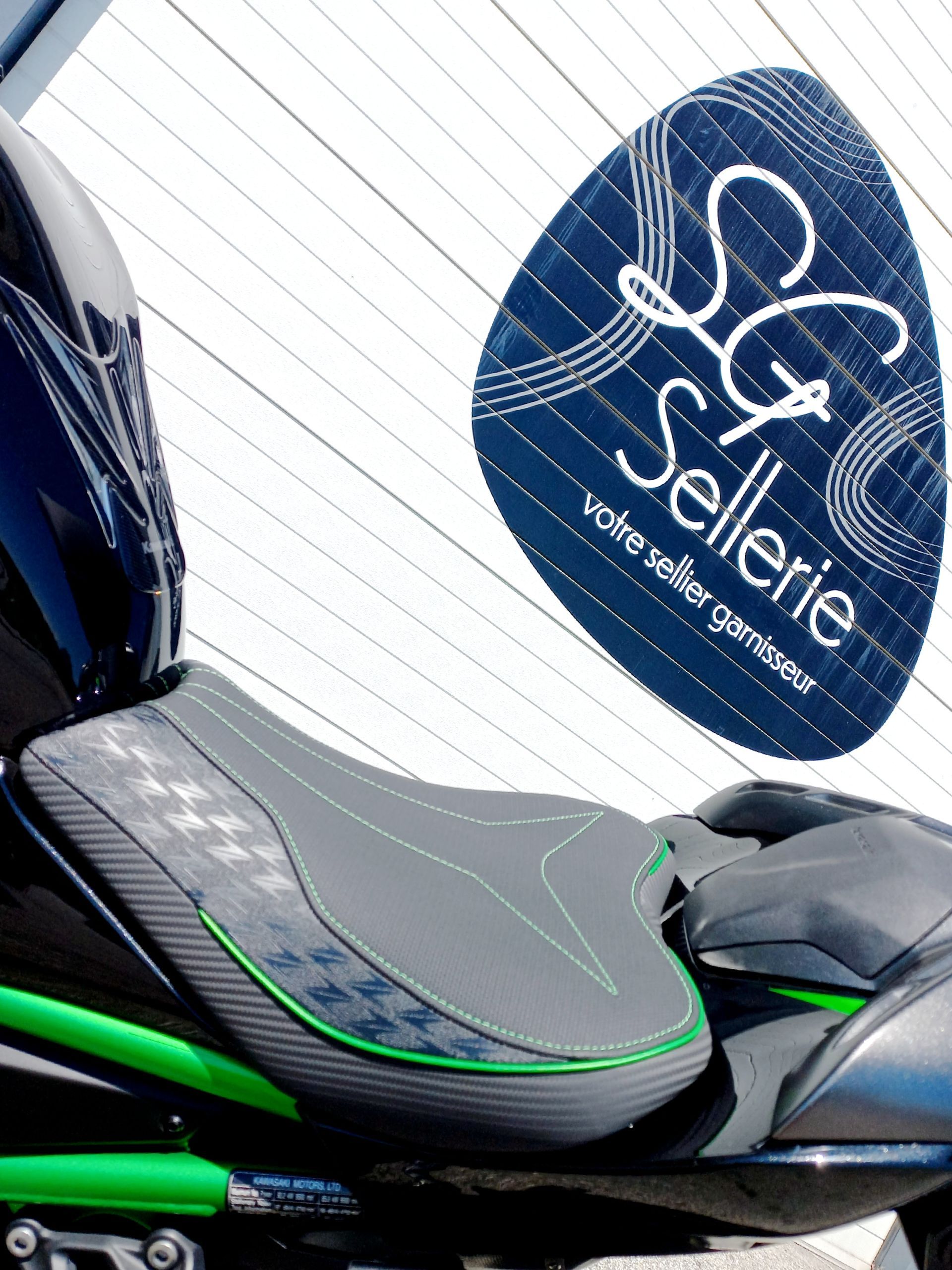 Gros plan sur une selle de moto noire et verte avec le logo bleu SG Sellerie en arrière-plan