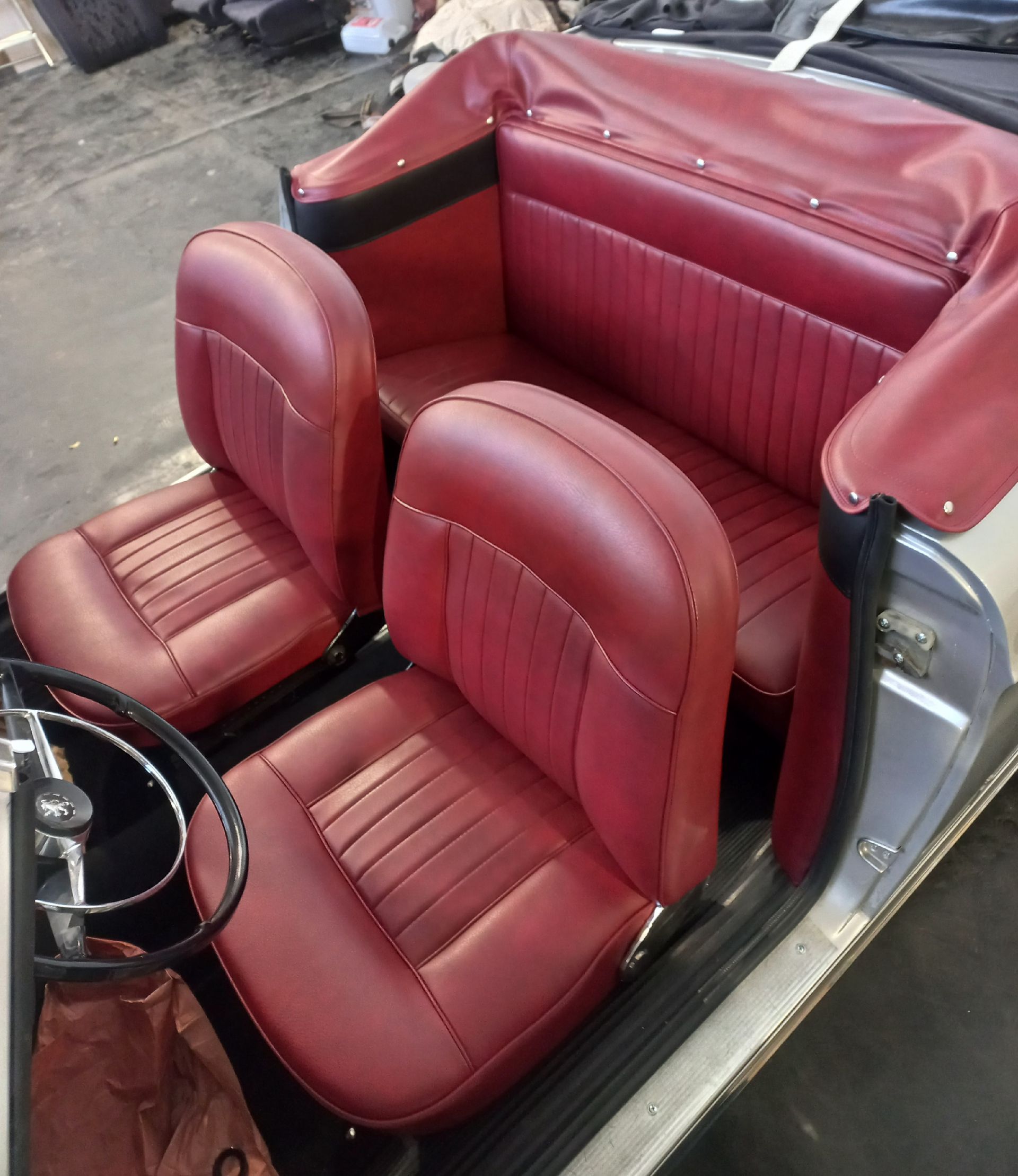 Deux sièges auto en cuir rouge dans l'intérieur d'un véhicule ancien, avec un volant visible.