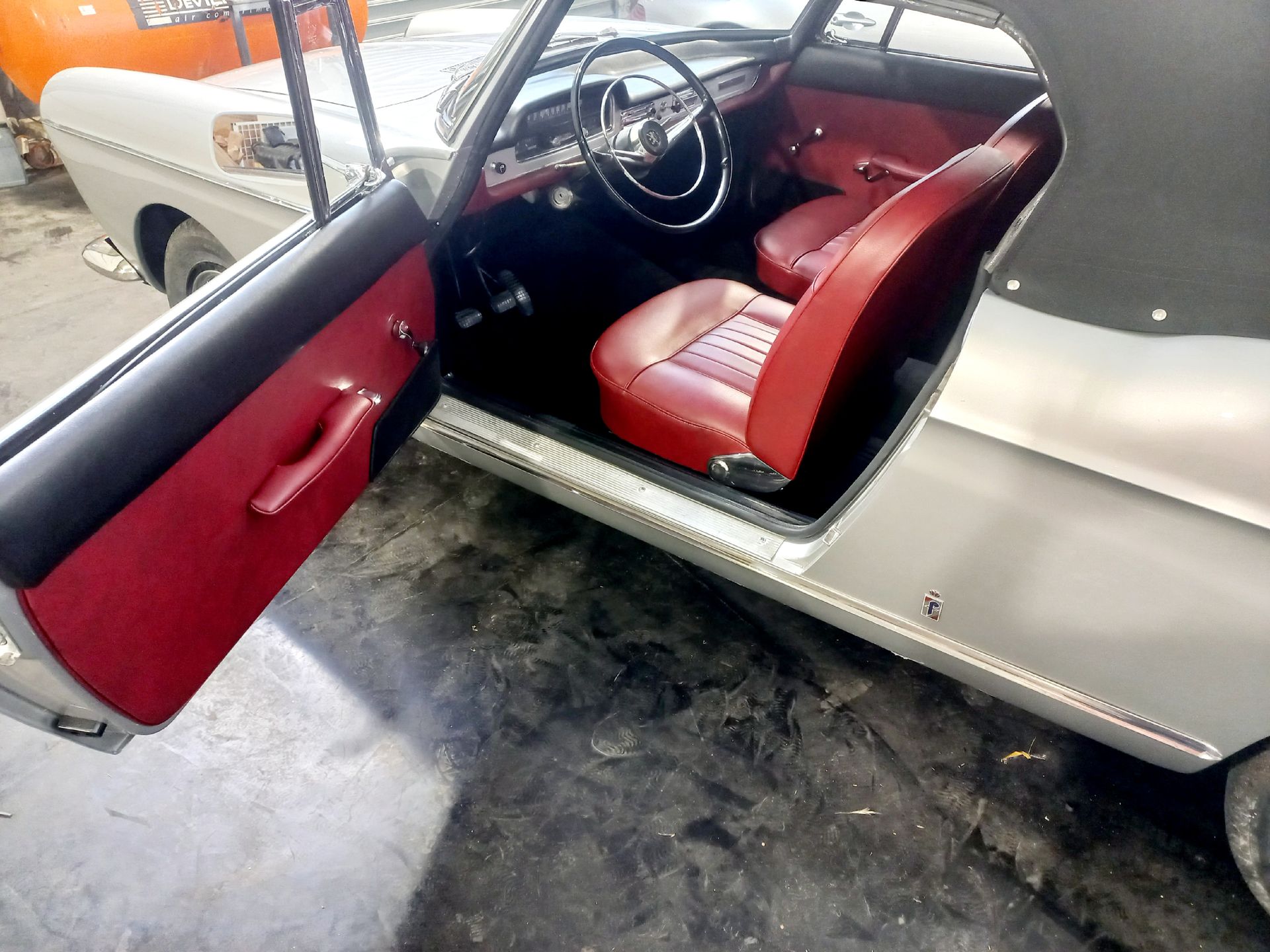 Portière de voiture ouverte, révélant des sièges intérieurs rouges et un volant dans un garage de voitures classiques