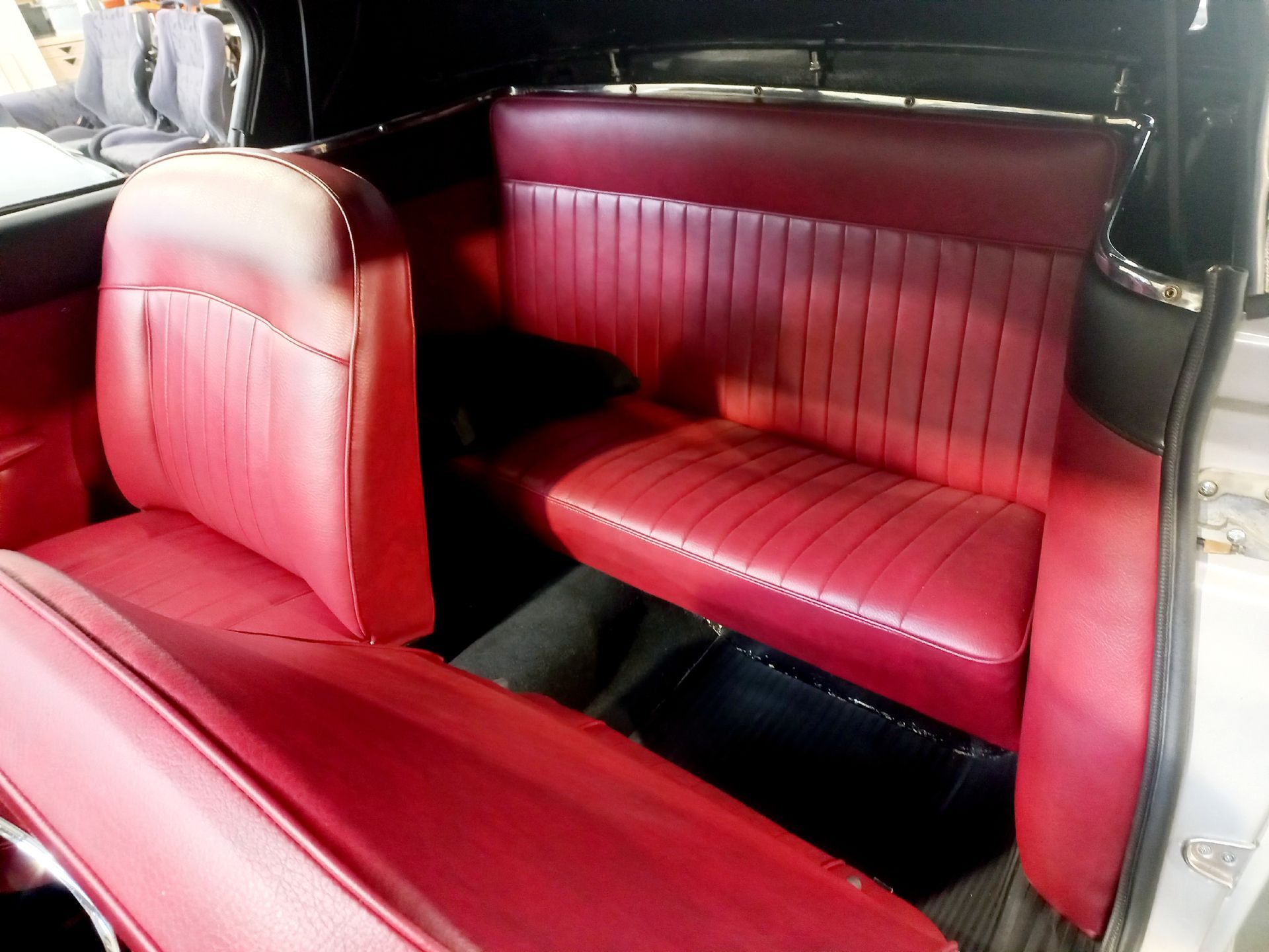 Intérieur en cuir rouge avec banquette arrière et siège avant assorti dans un véhicule ancien.