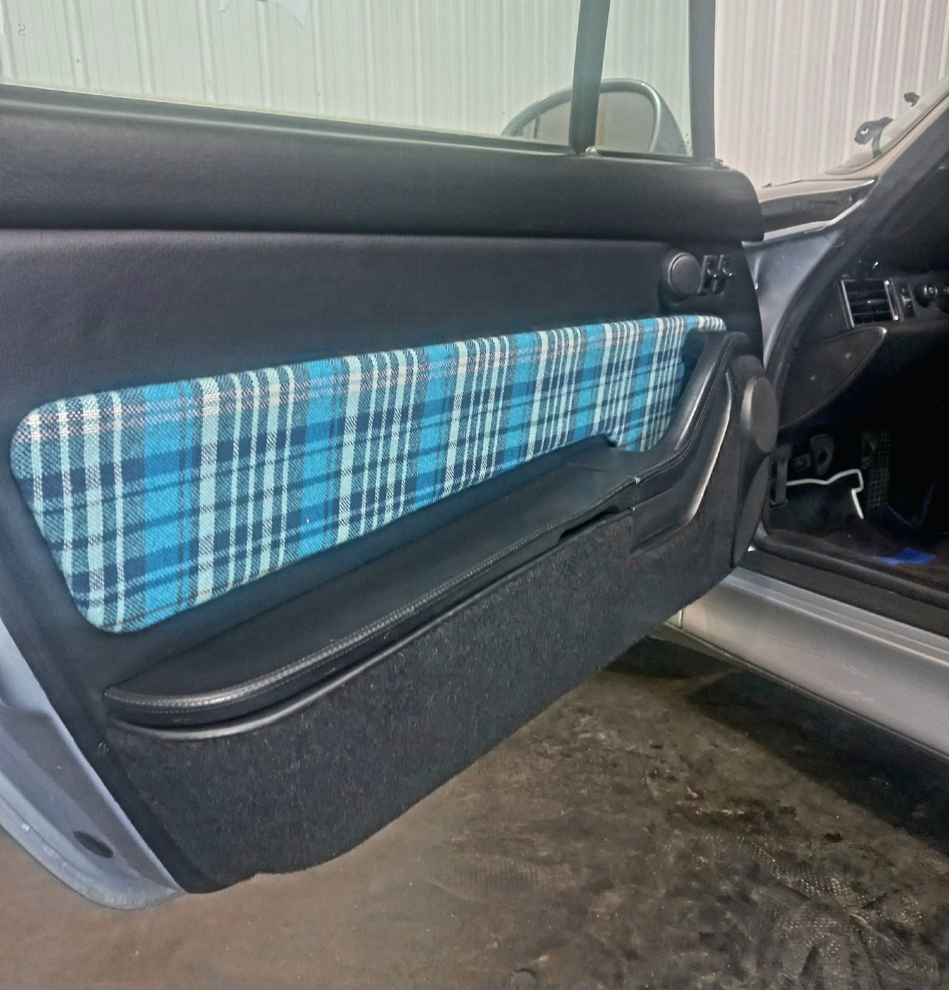 Panneau de portière de voiture avec insert en tissu à carreaux bleus et garniture noire, ouvert dans un garage