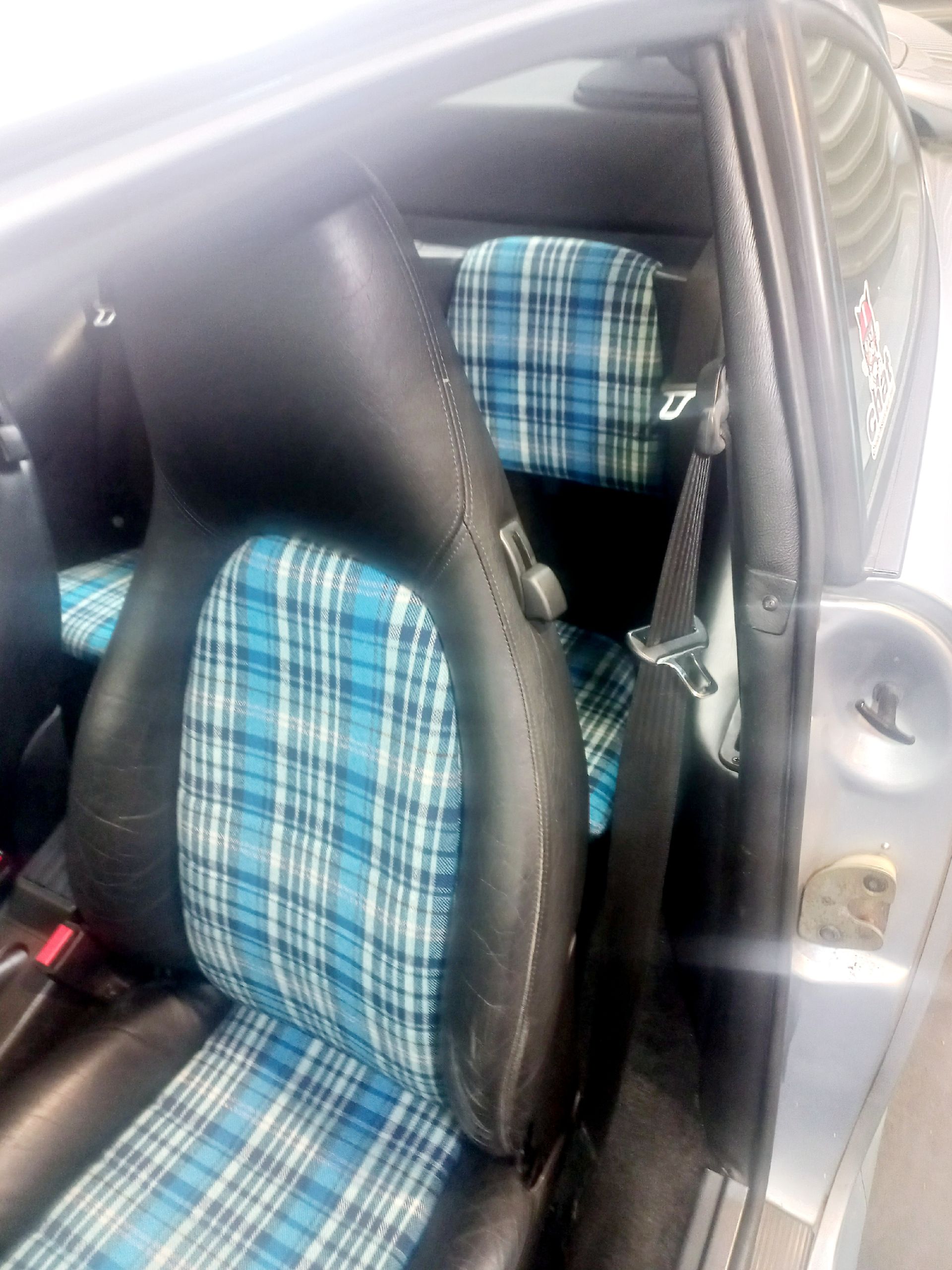 Deux sièges auto bleus à carreaux à l'intérieur d'un véhicule argenté, vus à travers la porte ouverte