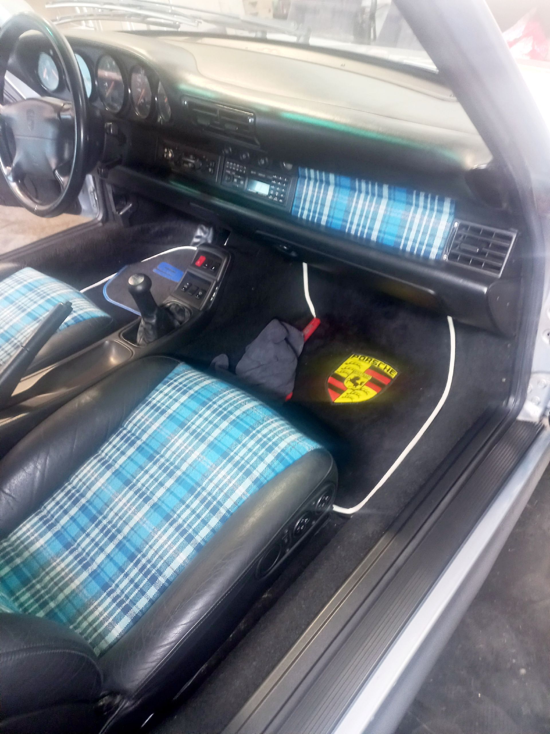 Intérieur de voiture avec sièges à carreaux bleus, volant et tableau de bord noir.