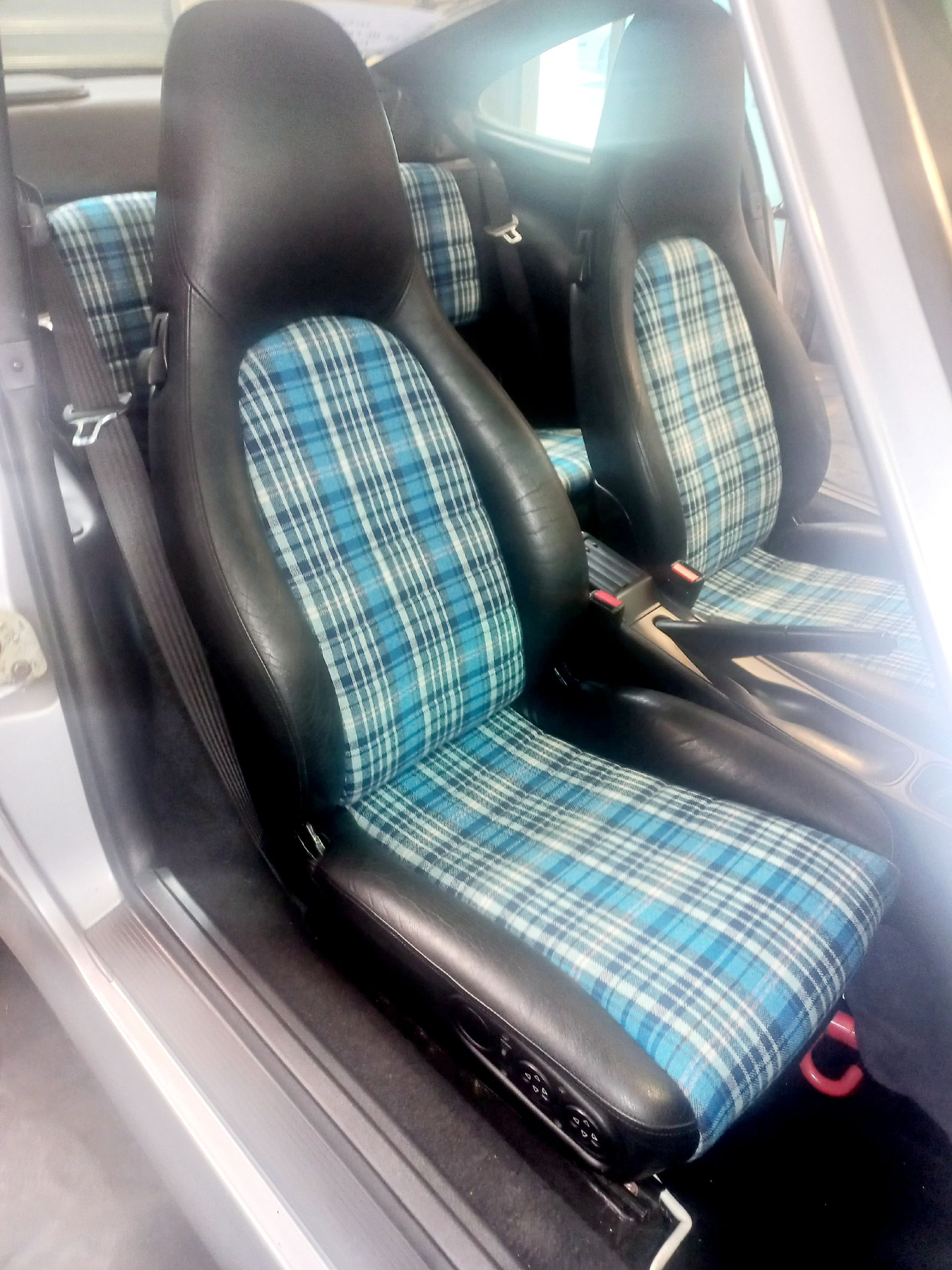 Intérieur de voiture avec sièges baquets avant à carreaux bleus et sellerie noire.