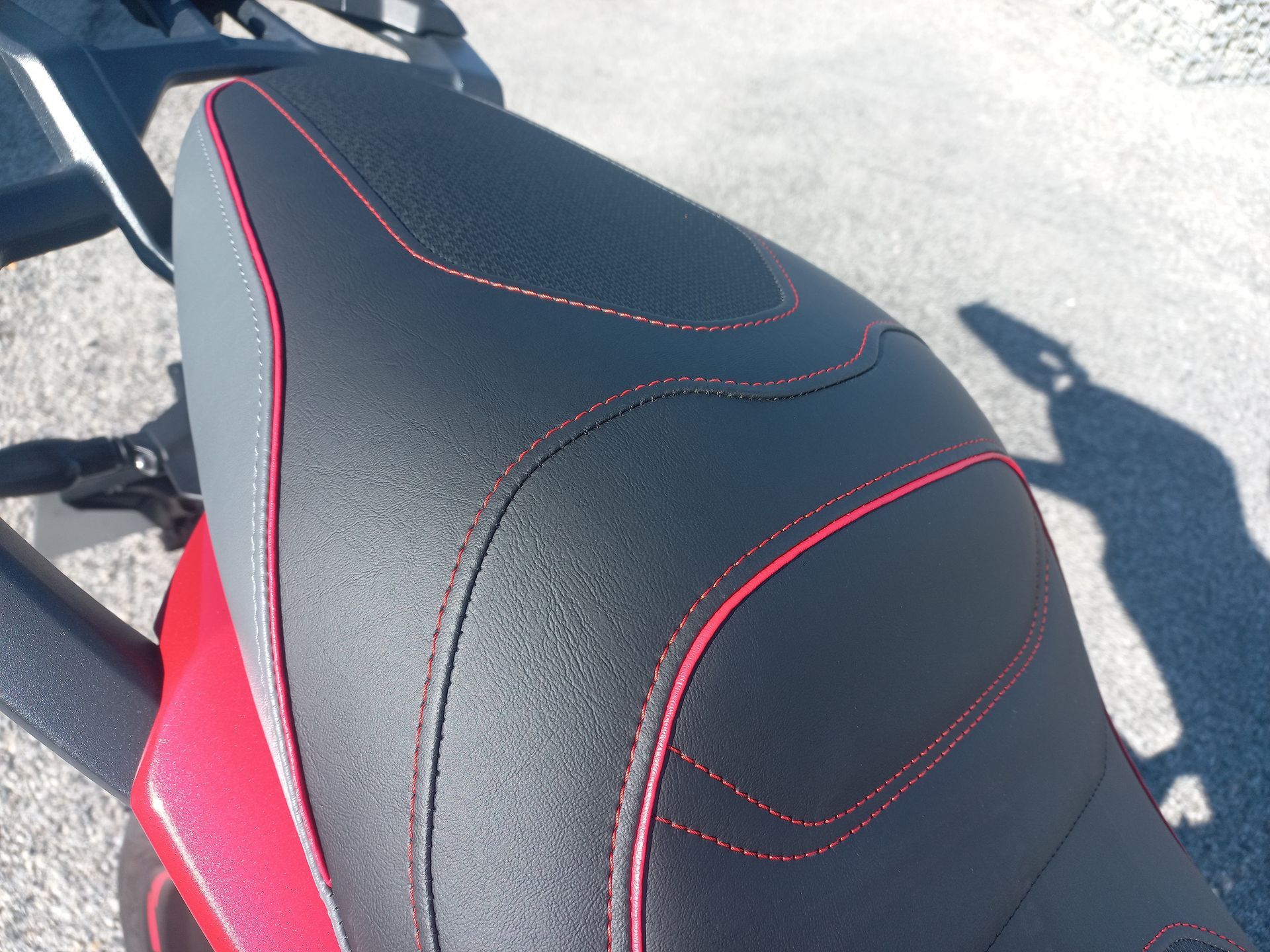 Gros plan sur une selle de moto noire à coutures rouges en plein soleil