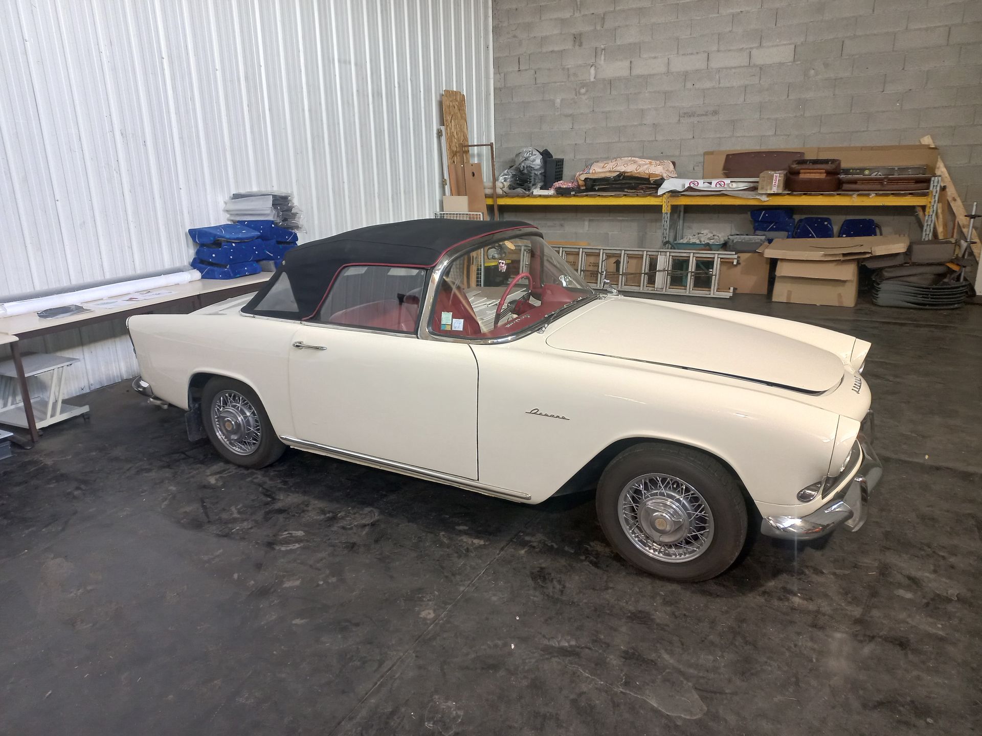 Voiture décapotable blanche vintage garée dans un garage intérieur, avec une capote noire.