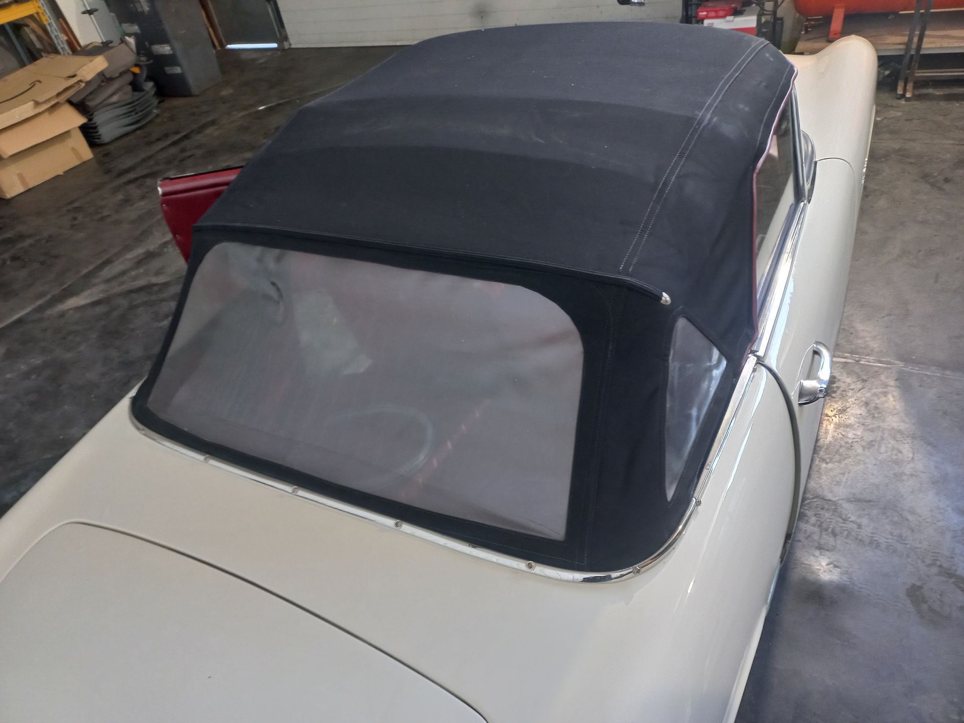Cabriolet blanc à capote noire garé dans un garage, vu du dessus.