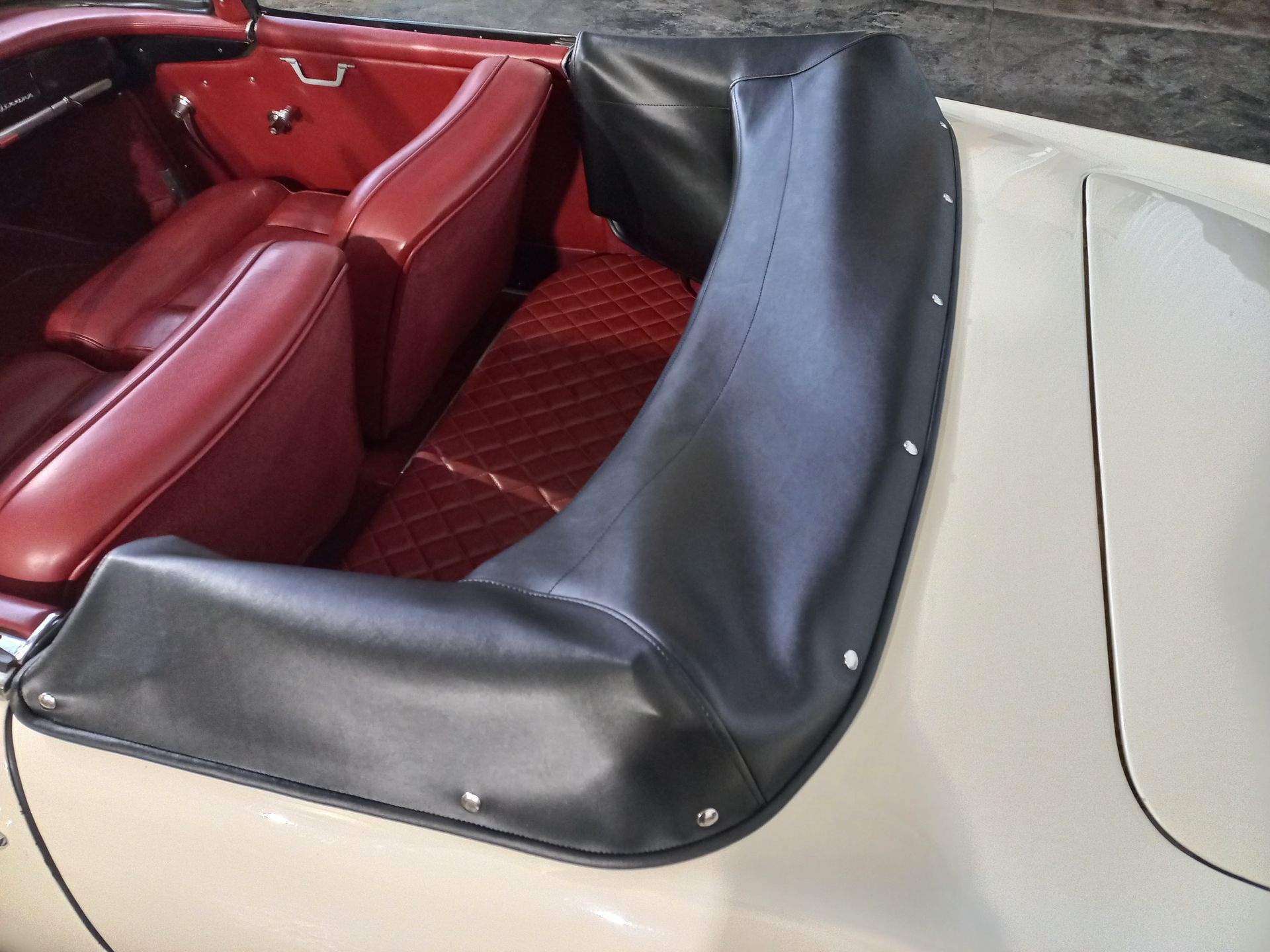 Voiture décapotable avec capote noire, extérieur crème et intérieur rouge.
