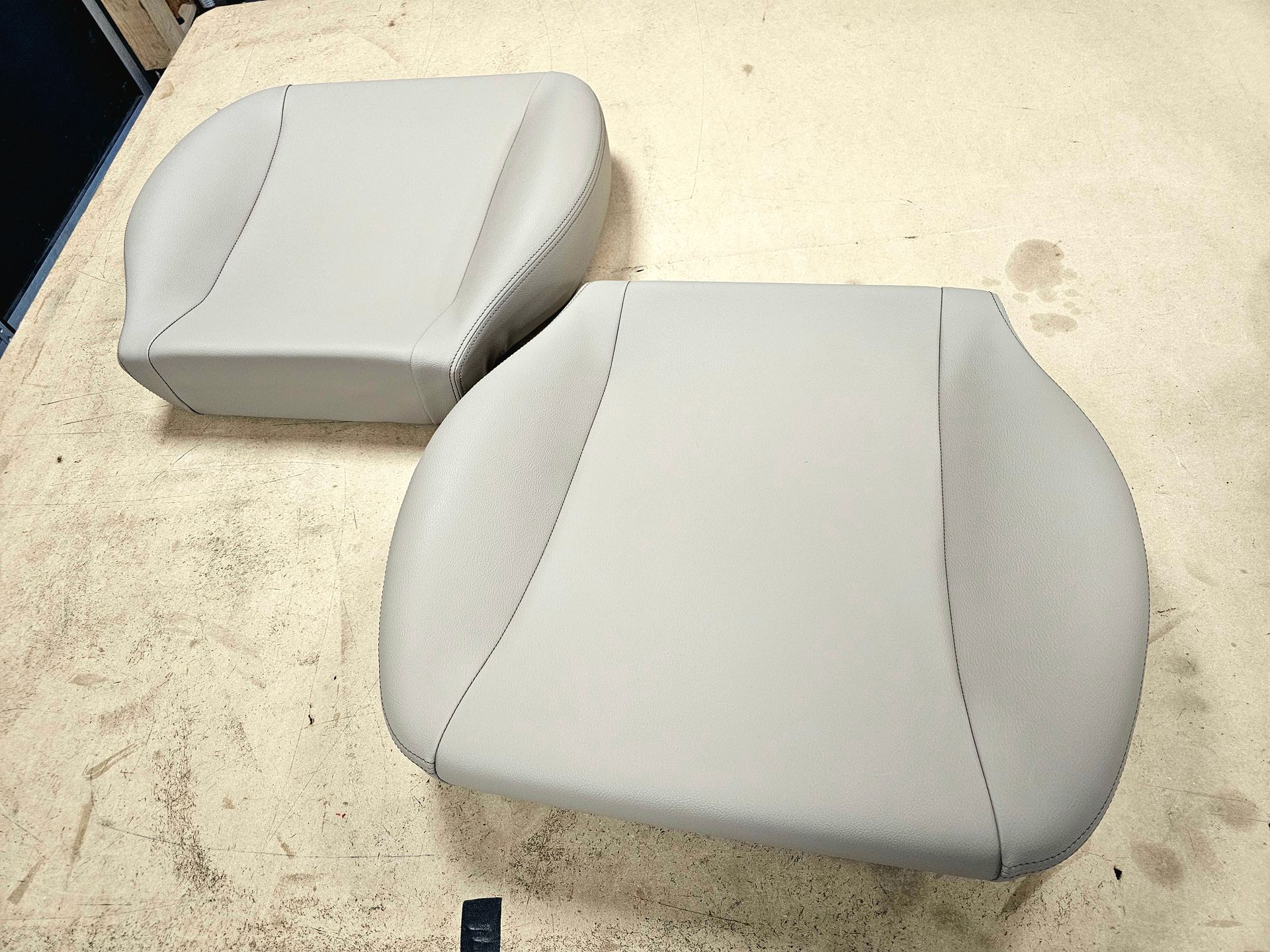 Deux coussins de siège gris clair recouverts de tissu sur un sol beige usé.