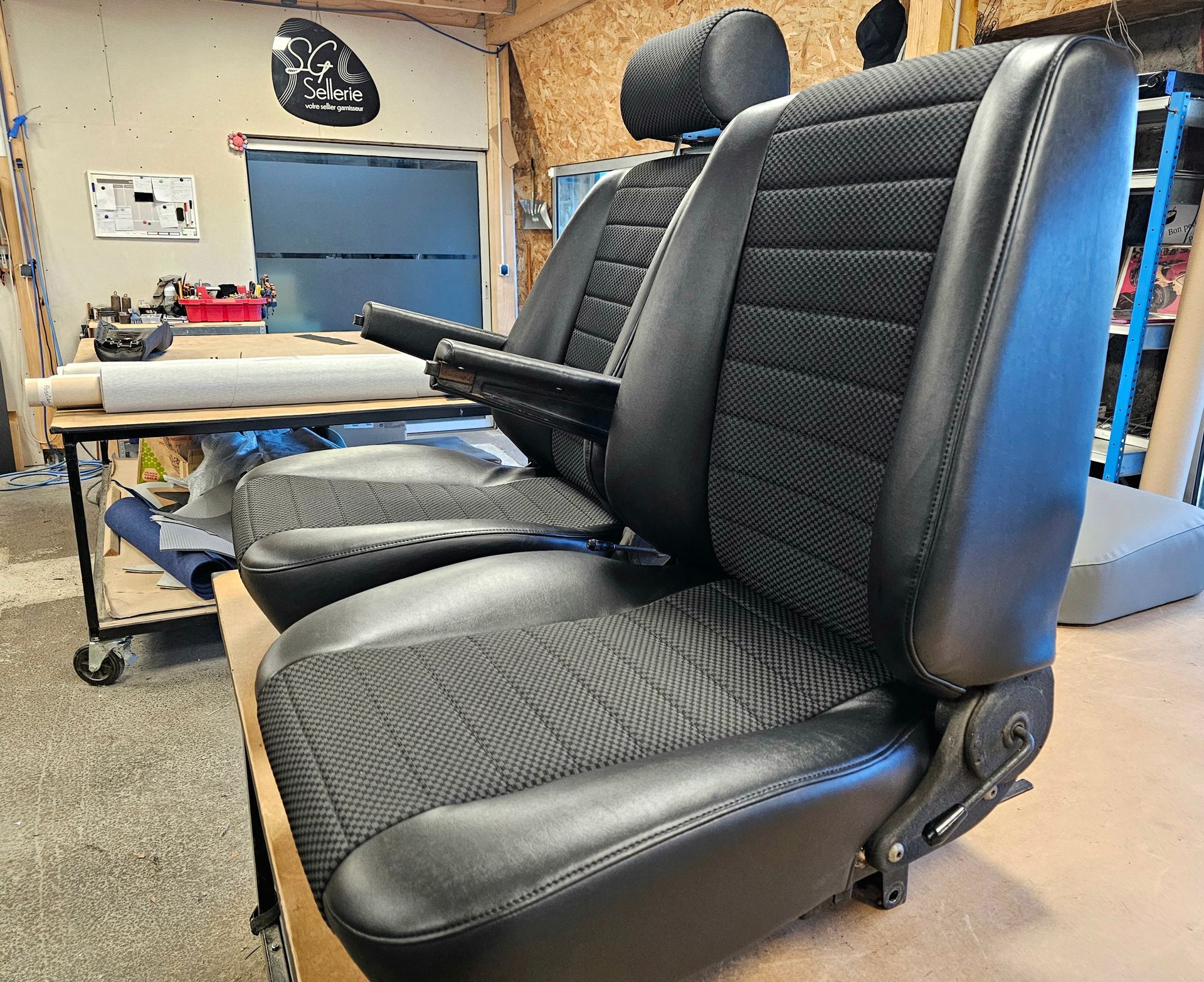 Deux fauteuils noirs inclinables dans un atelier, un accoudoir relevé.