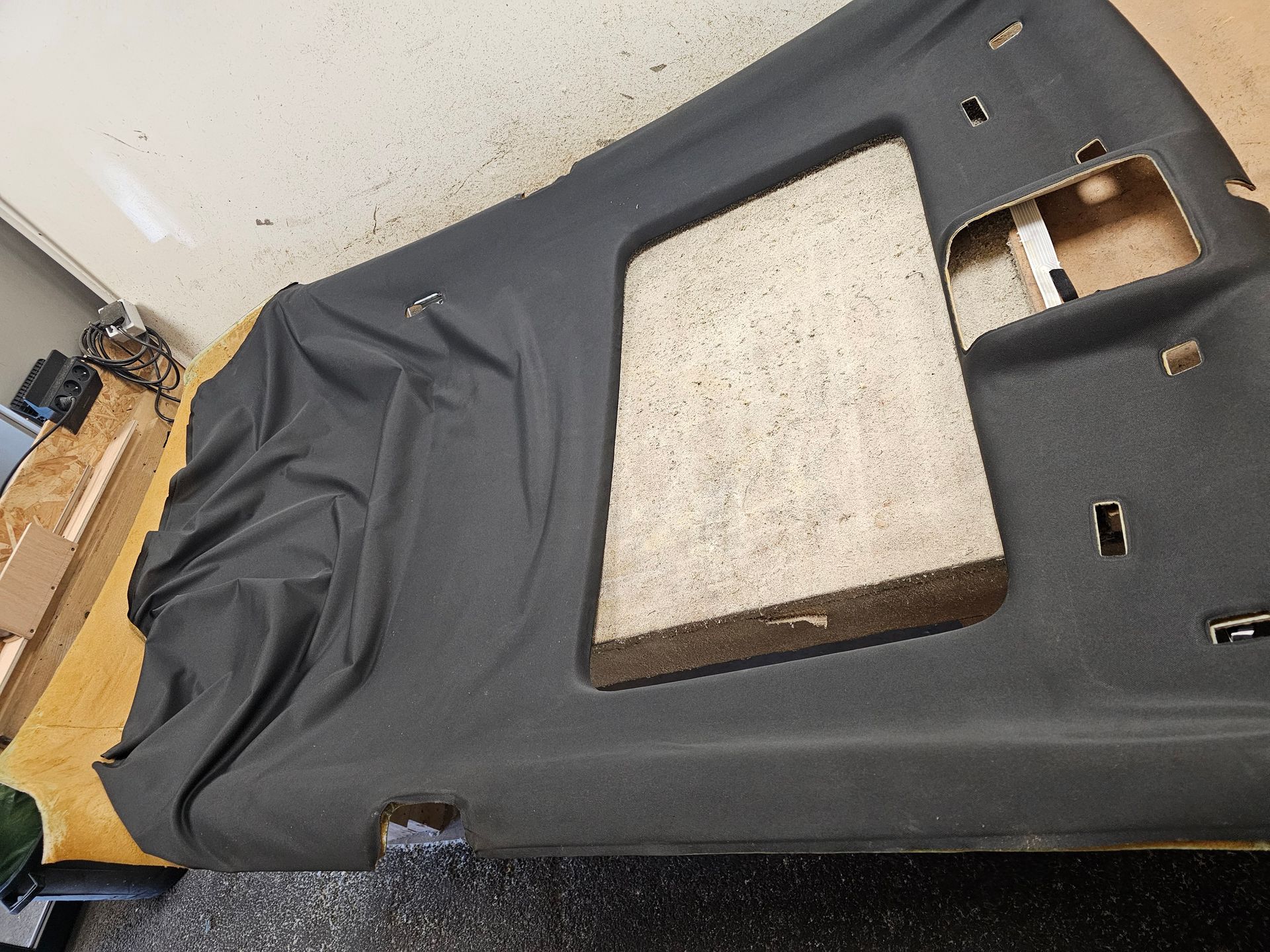 Panneau de garniture de toit de voiture en tissu noir avec une grande ouverture, posé sur un établi.