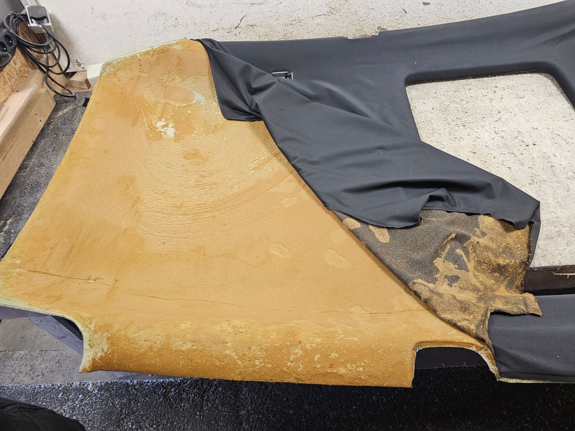 Un morceau de rembourrage en mousse jaune avec un tissu noir déchiré, posé au sol, présentant des signes de dommages et d'usure.