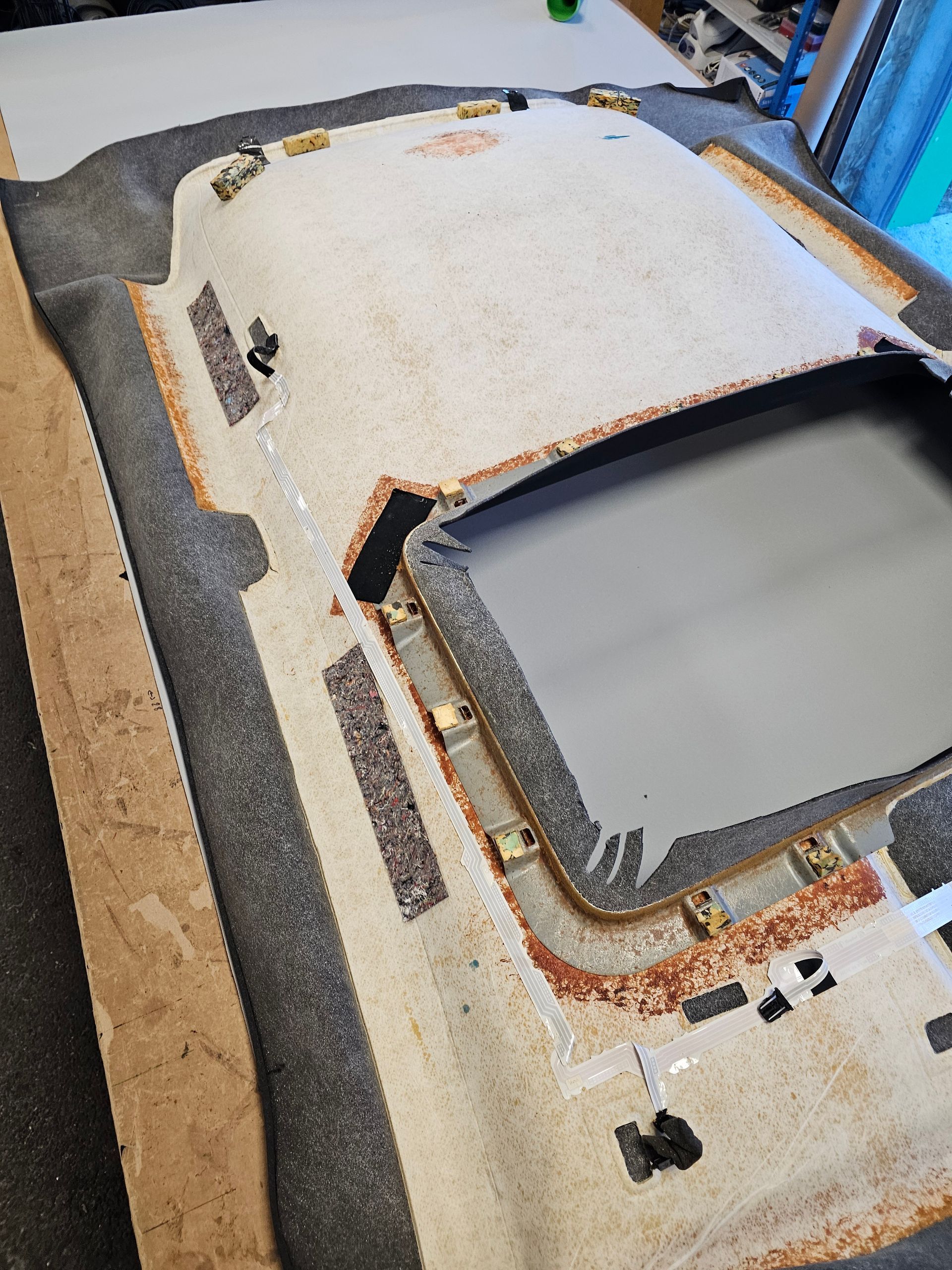 Un moule de carrosserie de véhicule recouvert d'une bâche beige avec des bordures noires, dans un atelier, vu de dessus.