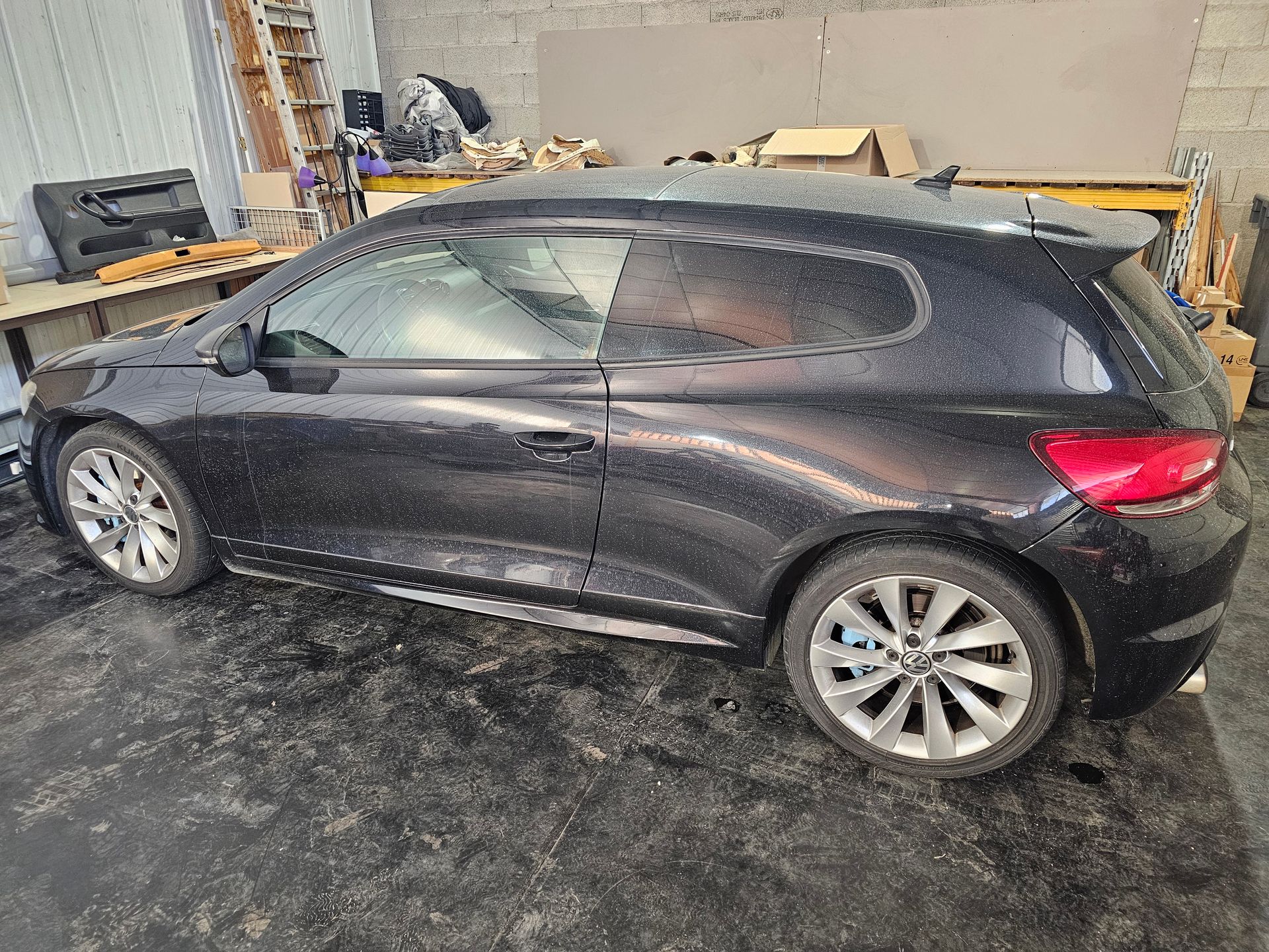Voiture à hayon noire deux portes dans un garage, présentant des dommages visibles à l'arrière et une portière cabossée.
