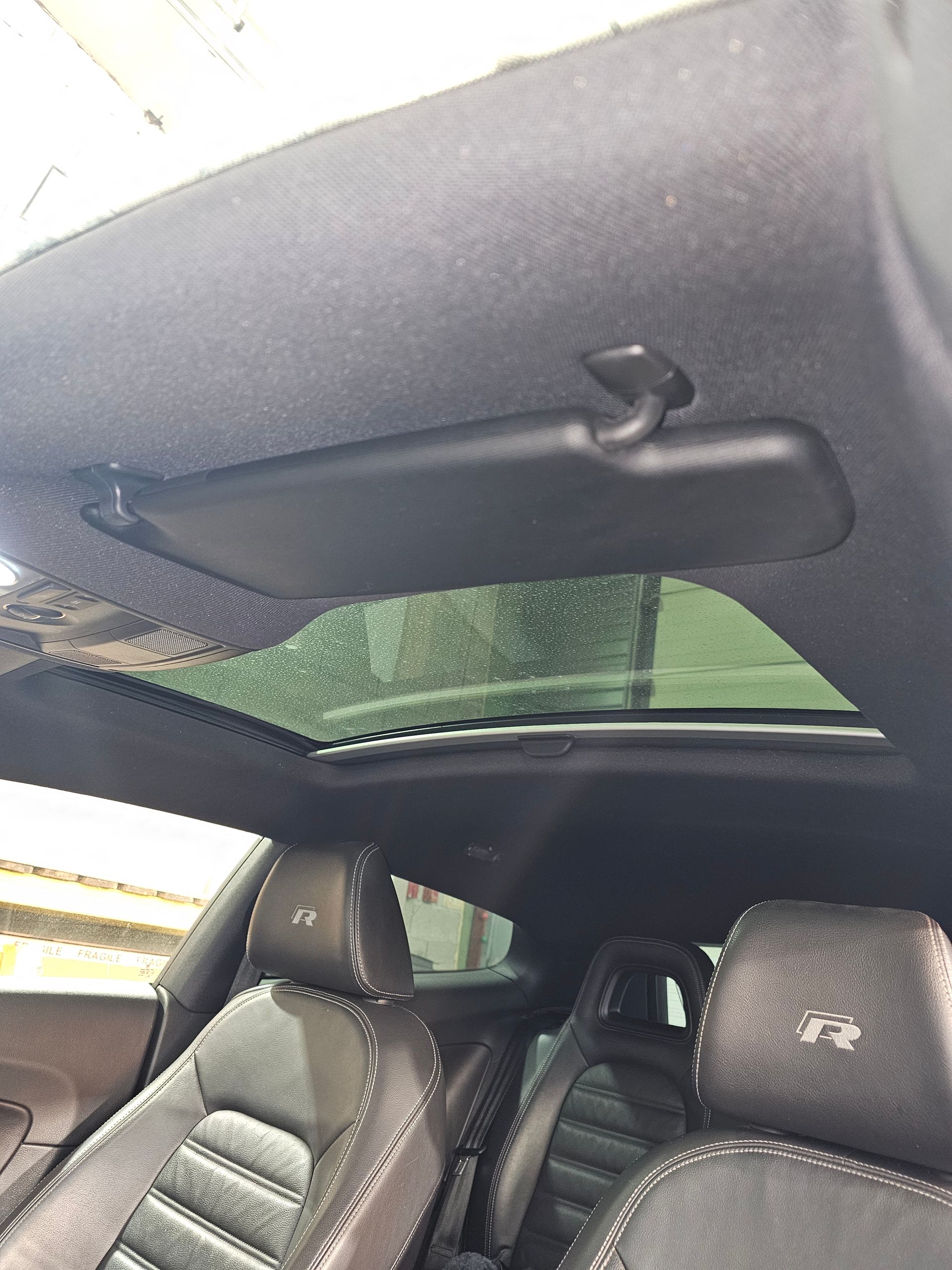 Intérieur de voiture avec toit ouvrant, sièges noirs et aileron arrière visible à travers la lunette arrière