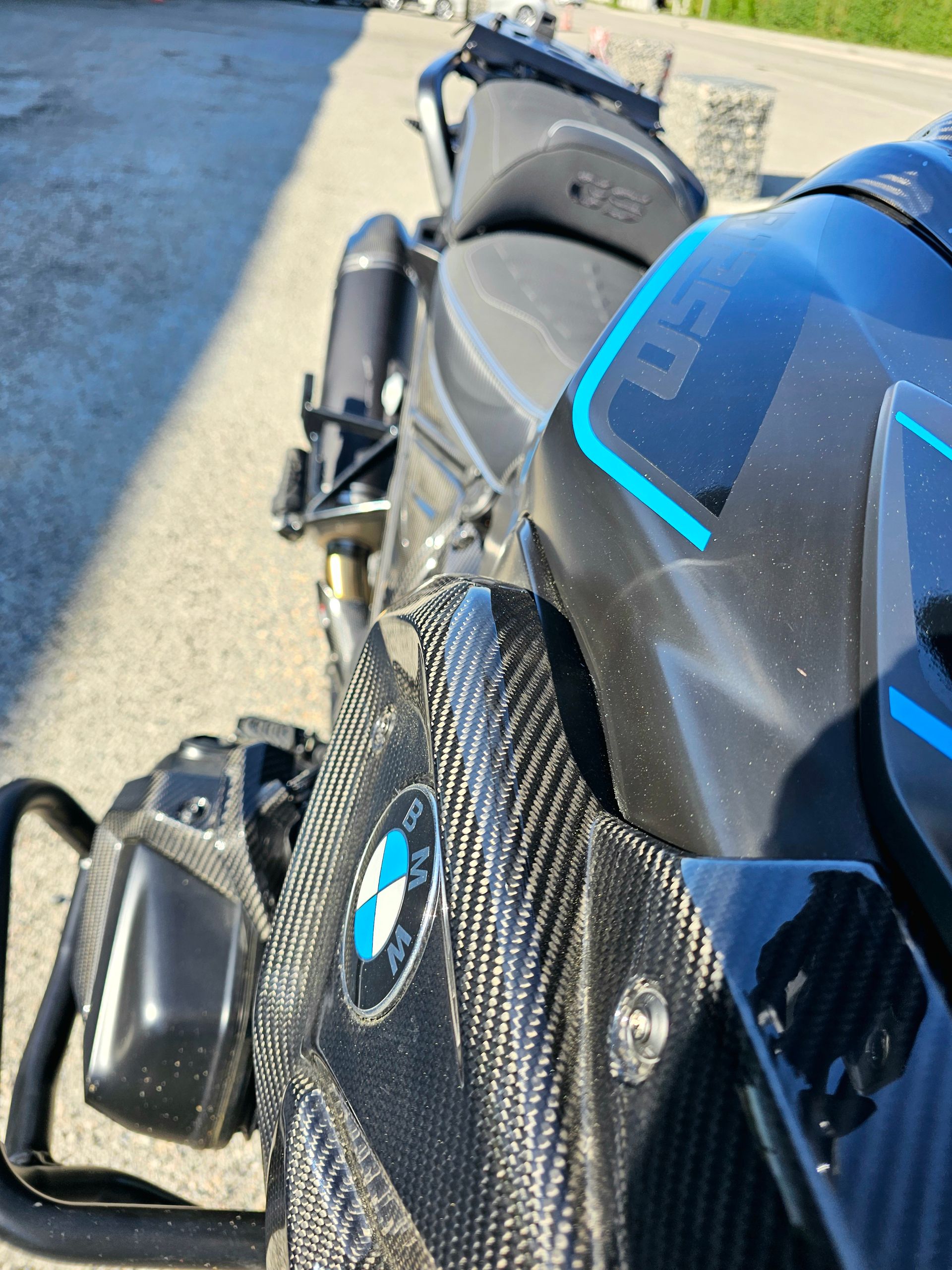 Gros plan sur une moto BMW noire avec des garnitures en fibre de carbone et des touches de bleu, garée à l'extérieur sur le trottoir.