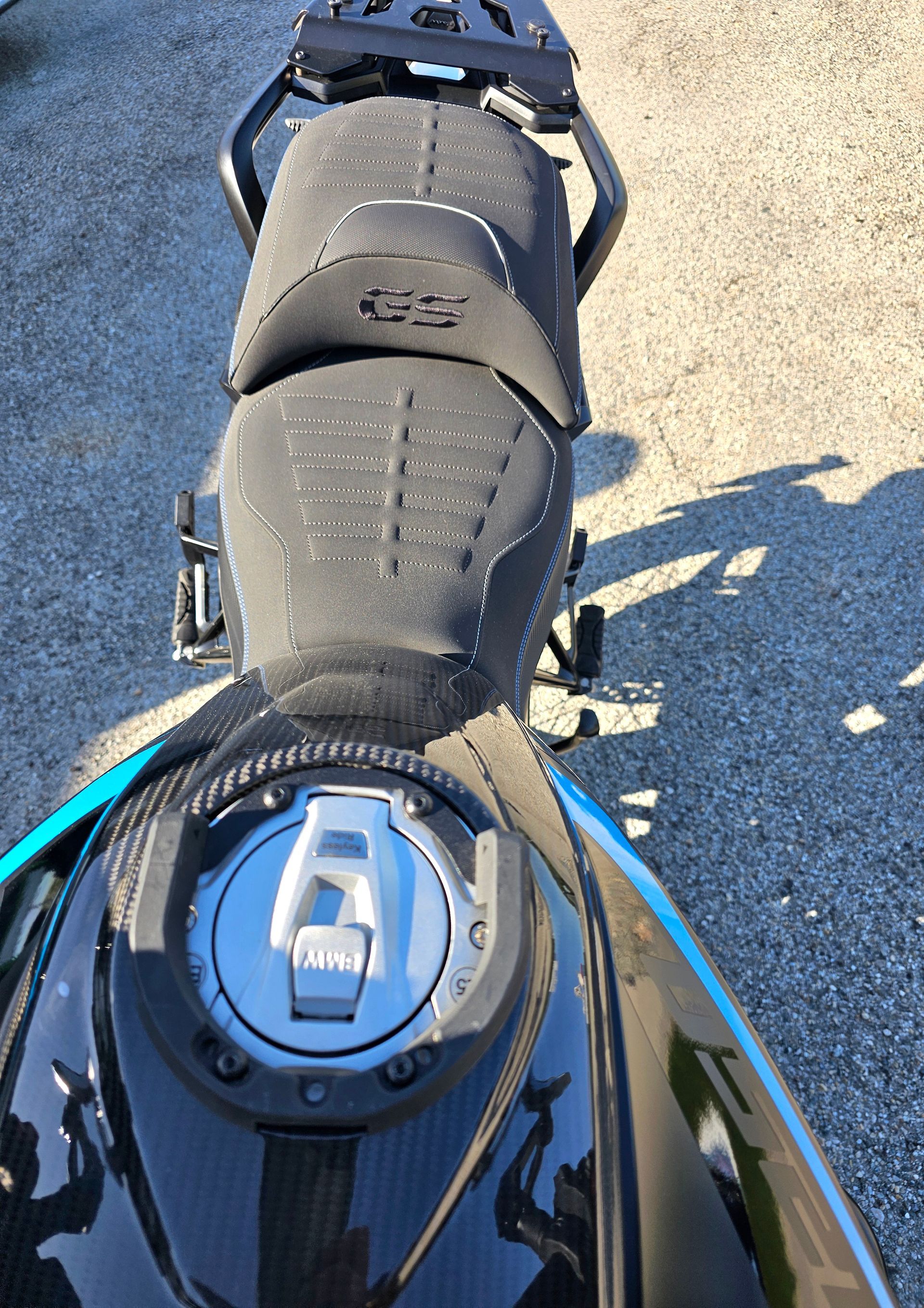 Vue de dessus d'une selle de moto noire et d'un réservoir d'essence sur du gravier, avec des touches de bleu.