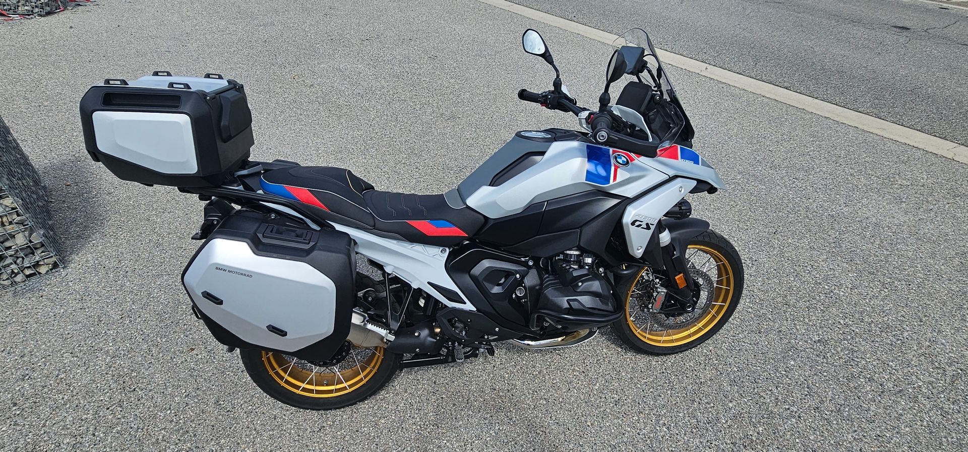 Moto de sport touring blanche et noire avec valises latérales, garée en bord de route asphaltée