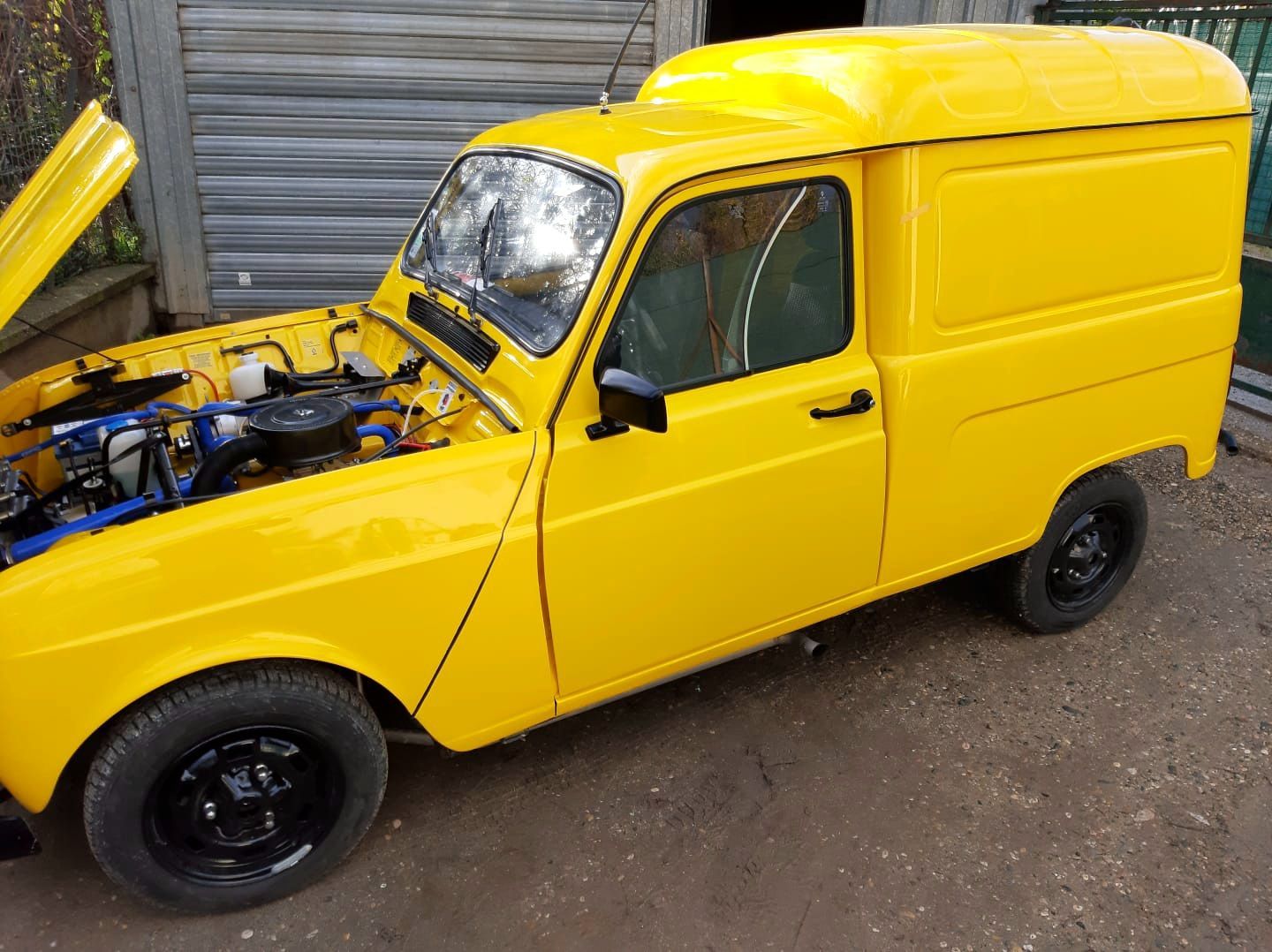 Fourgonnette jaune, capot ouvert, moteur visible, garée dans une allée.