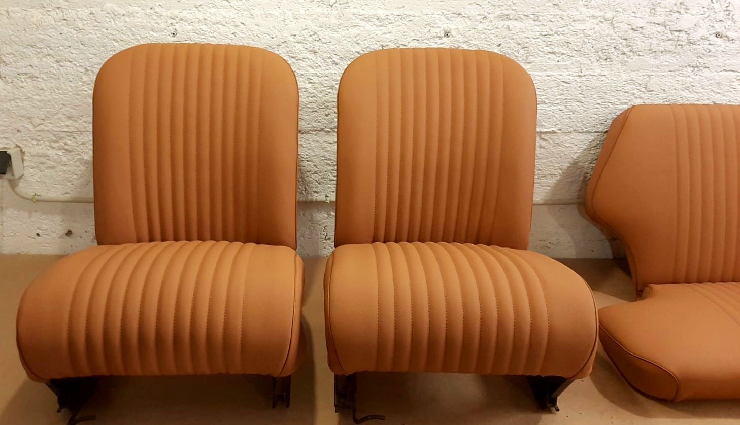 Trois fauteuils lounges orange capitonnés sont adossés à un mur blanc texturé ; l'un d'eux est partiellement visible à droite.
