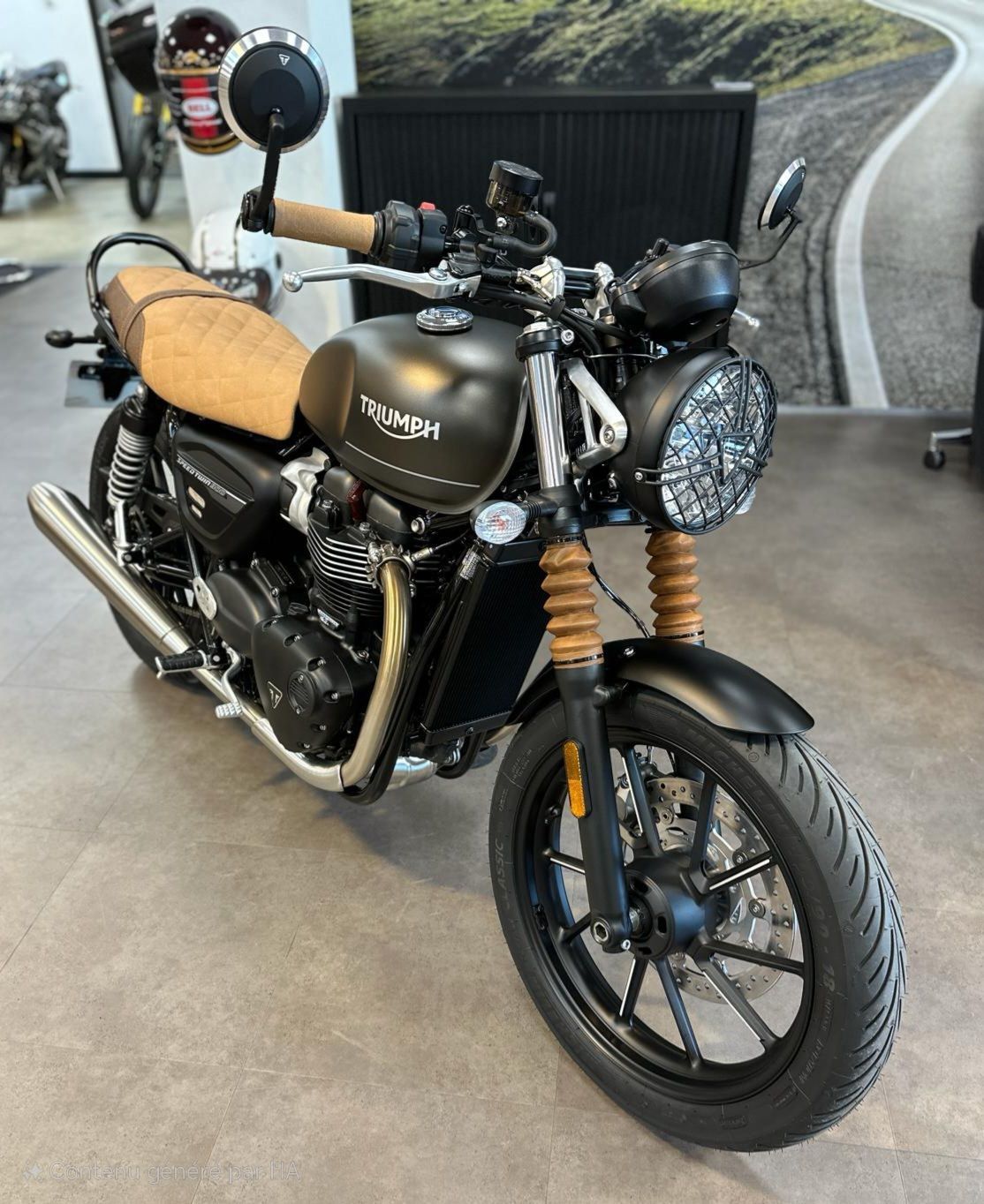 Moto Triumph noire dans un showroom, avec phare rond, selle beige et roues noires.