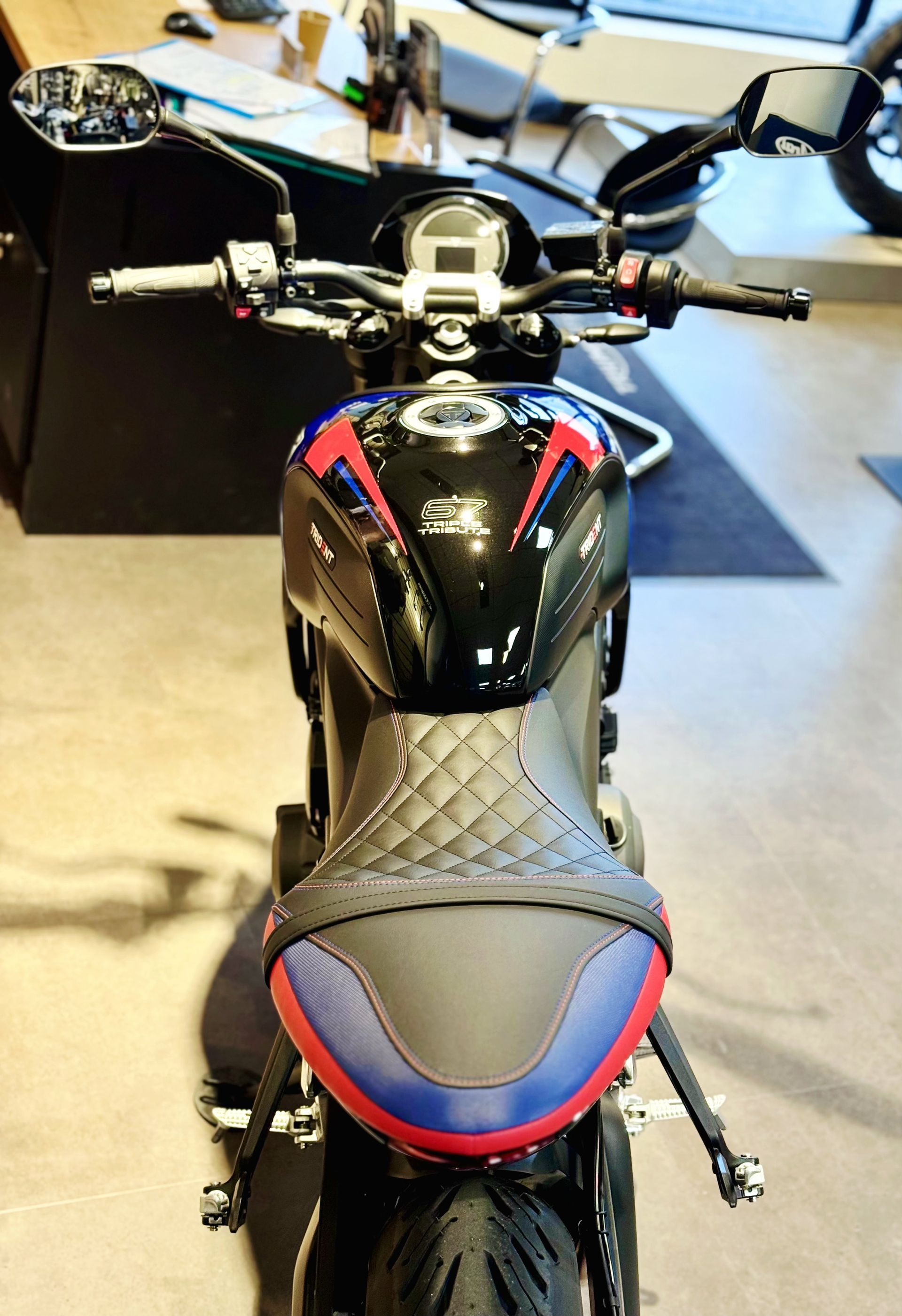 Moto noire avec des accents rouges et bleus, vue de l'arrière dans un showroom intérieur
