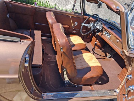 Intérieur de voiture en cuir marron avec sièges avant et tableau de bord visibles, vu depuis la porte ouverte