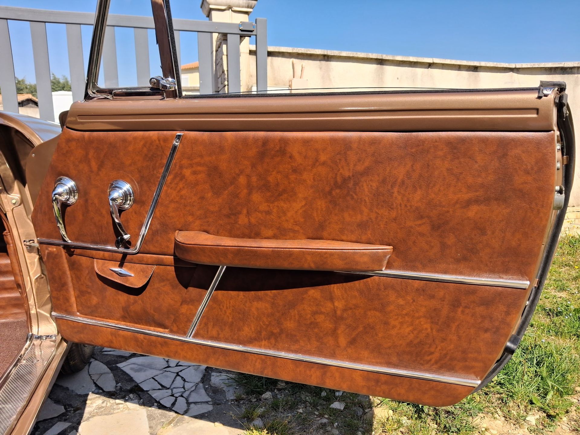 Panneau de porte de voiture en cuir marron avec poignée et accoudoir chromés, présenté à l'extérieur en plein soleil