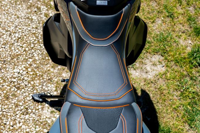 Vue de dessus d'une selle de moto noire avec des surpiqûres orange sur du gravier