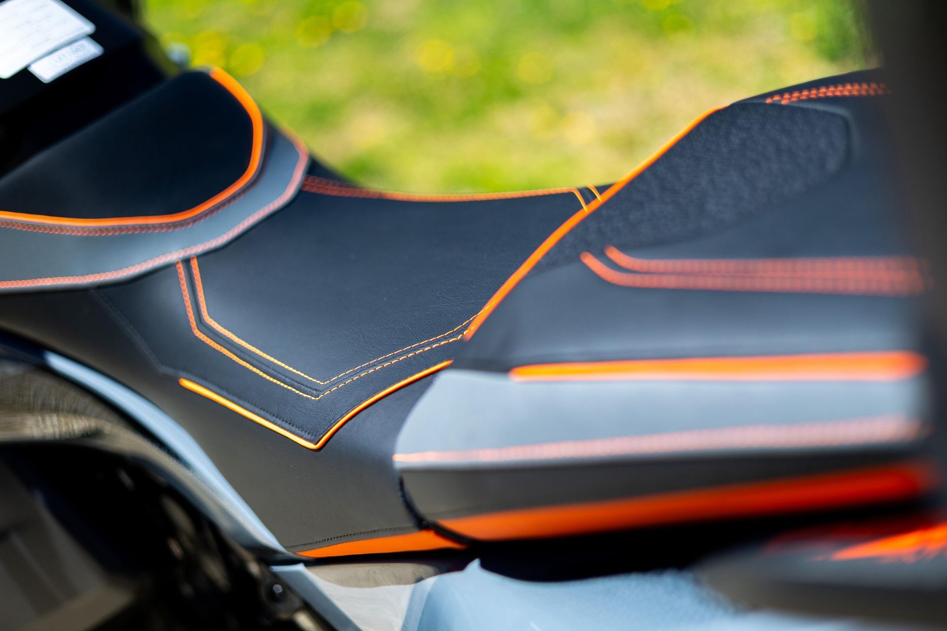 Gros plan sur une selle de moto noire avec passepoil et surpiqûres orange.
