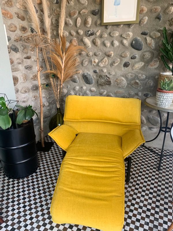 Fauteuil jaune dans une pièce aux murs de pierre avec des plantes en pot et un sol carrelé noir et blanc
