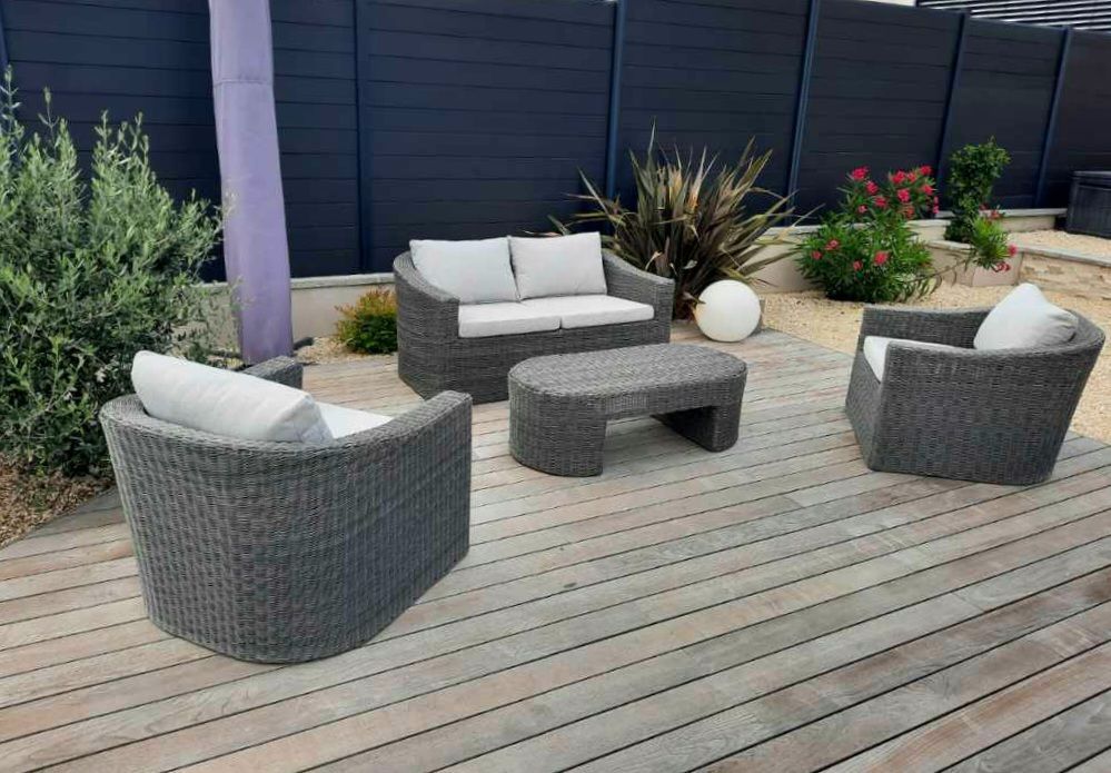 Terrasse extérieure avec chaises longues en osier gris, table assortie et plantes en pot sur une terrasse en bois
