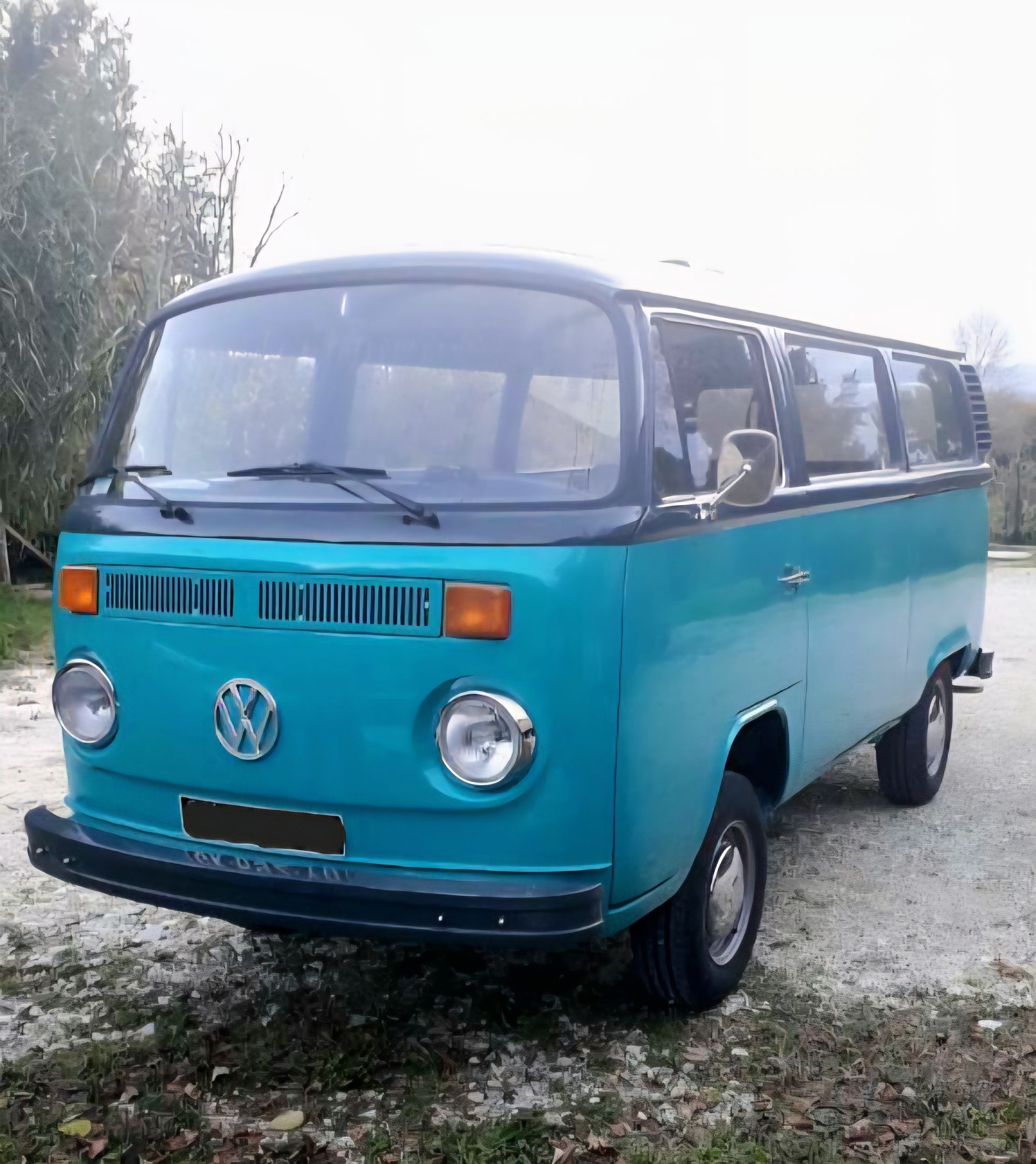 Une camionnette Volkswagen vintage turquoise est garée à l'extérieur sur un chemin de gravier.