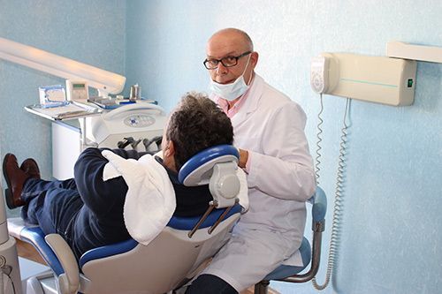 Un dentista examina a un paciente en el sillón dental, con sus instrumentos y un teléfono fijo en la pared cerca.