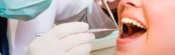 Odontólogo examinando la boca abierta de un paciente con un espejo dental y un instrumento durante una revisión.