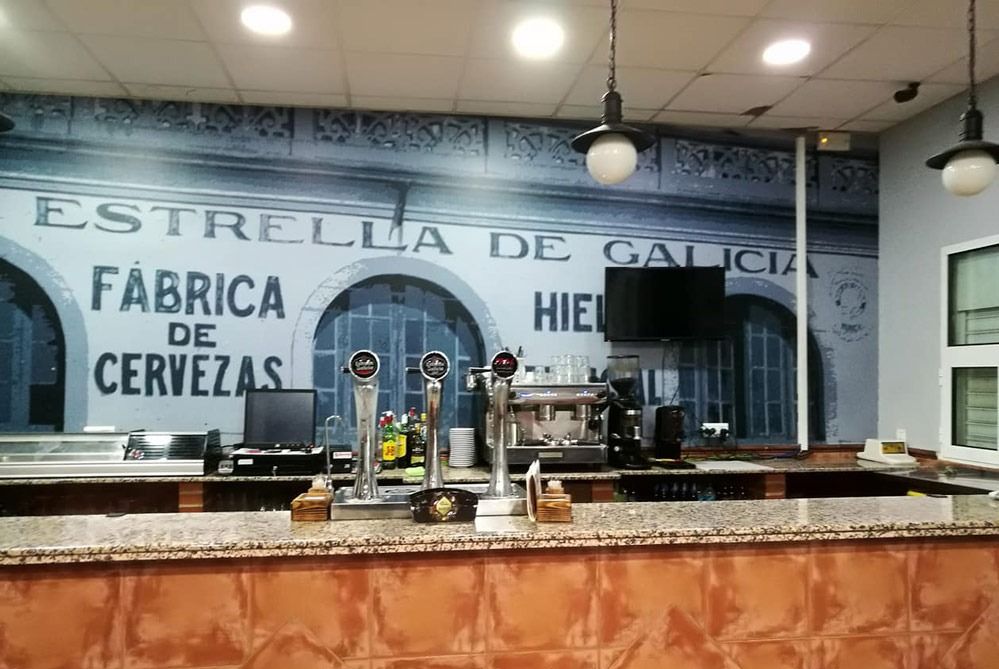 Interior of a bar with a beer tap counter and a mural reading “Estrella de Galicia, Fábrica de Cervezas”