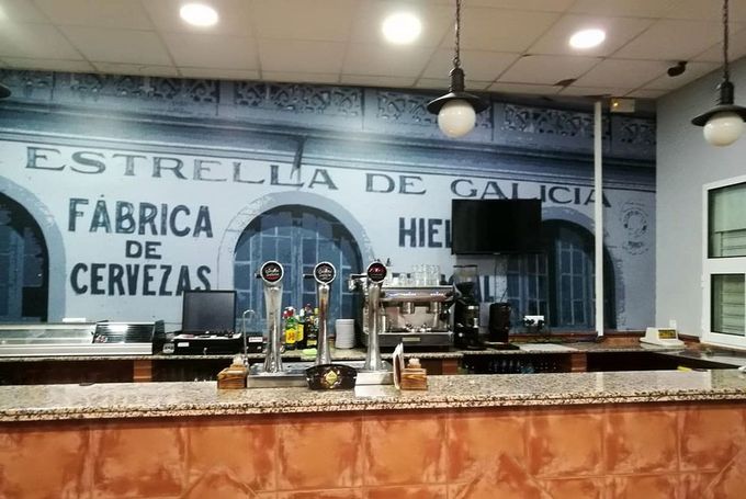 Interior of a bar with a beer tap counter and a mural reading “Estrella de Galicia, Fábrica de Cervezas”
