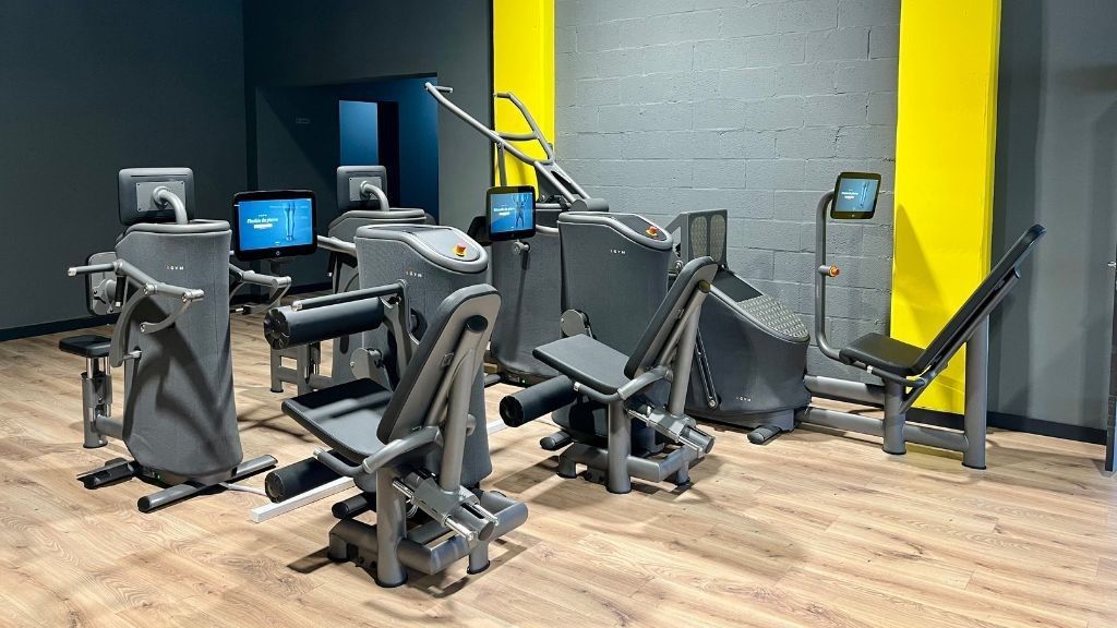 Aparatos de gimnasio en un moderno centro de fitness, sobre una pared amarilla y gris. Suelo de madera.