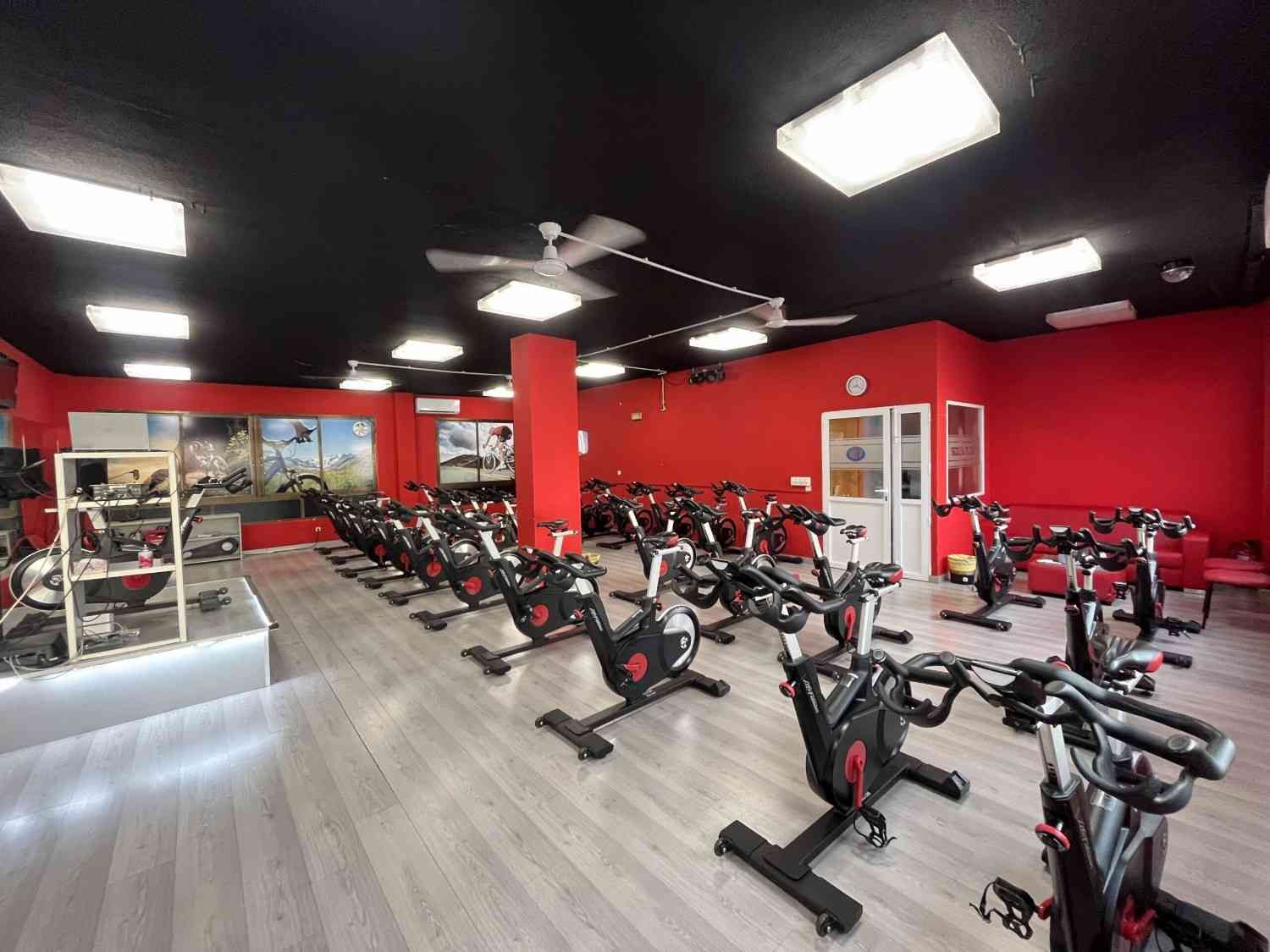 Estudio de clases de spinning con bicicletas estáticas, paredes rojas, techo negro y luces brillantes.