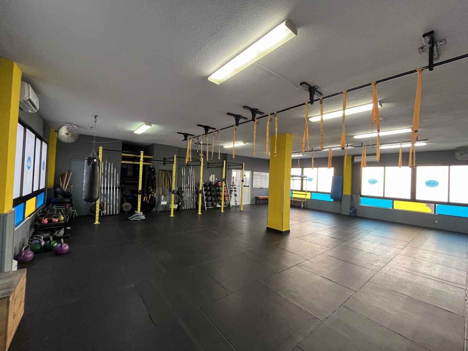 Interior de gimnasio con piso negro, detalles en amarillo, equipo de entrenamiento y correas para colgar.