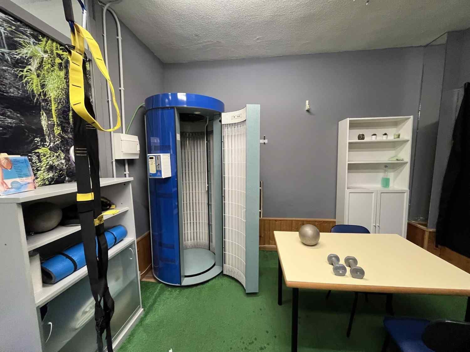 Una cabina de bronceado, equipos de gimnasio y estantes en una habitación.