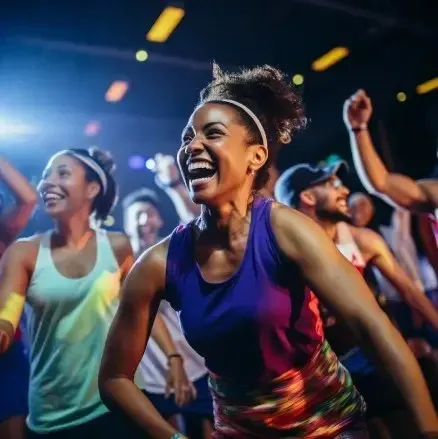 Gente bailando y sonriendo en la clase de fitness, ropa colorida, entorno oscuro.