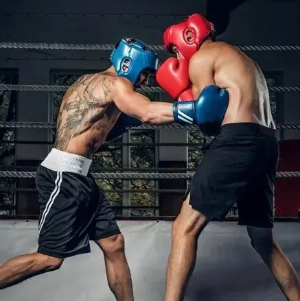 Dos boxeadores en un ring, con casco y guantes, lanzando golpes.