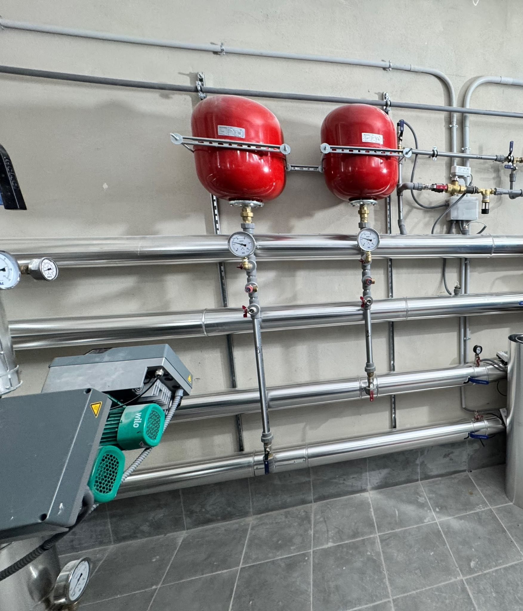 Depósitos de presión rojos y tuberías metálicas instalados en una pared de una sala de servicios industriales.