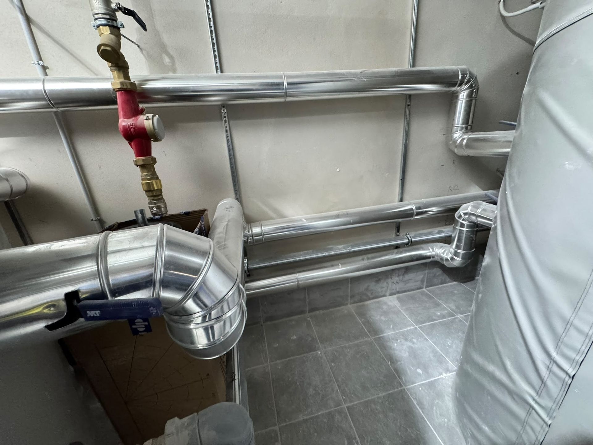 Conductos metálicos de climatización y tuberías aisladas junto a una pared alicatada en un cuarto de servicio