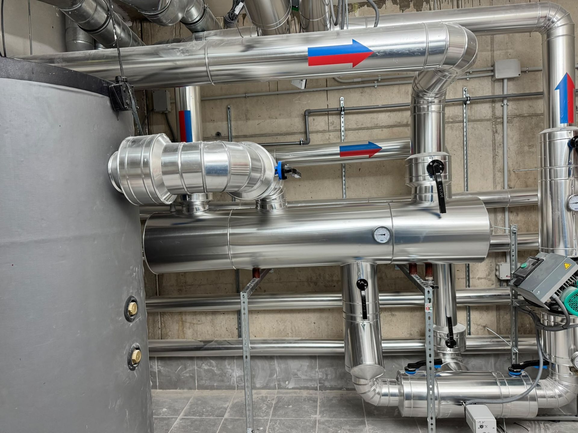 Tuberías industriales y conductos con flechas direccionales azules y rojas en una sala de máquinas