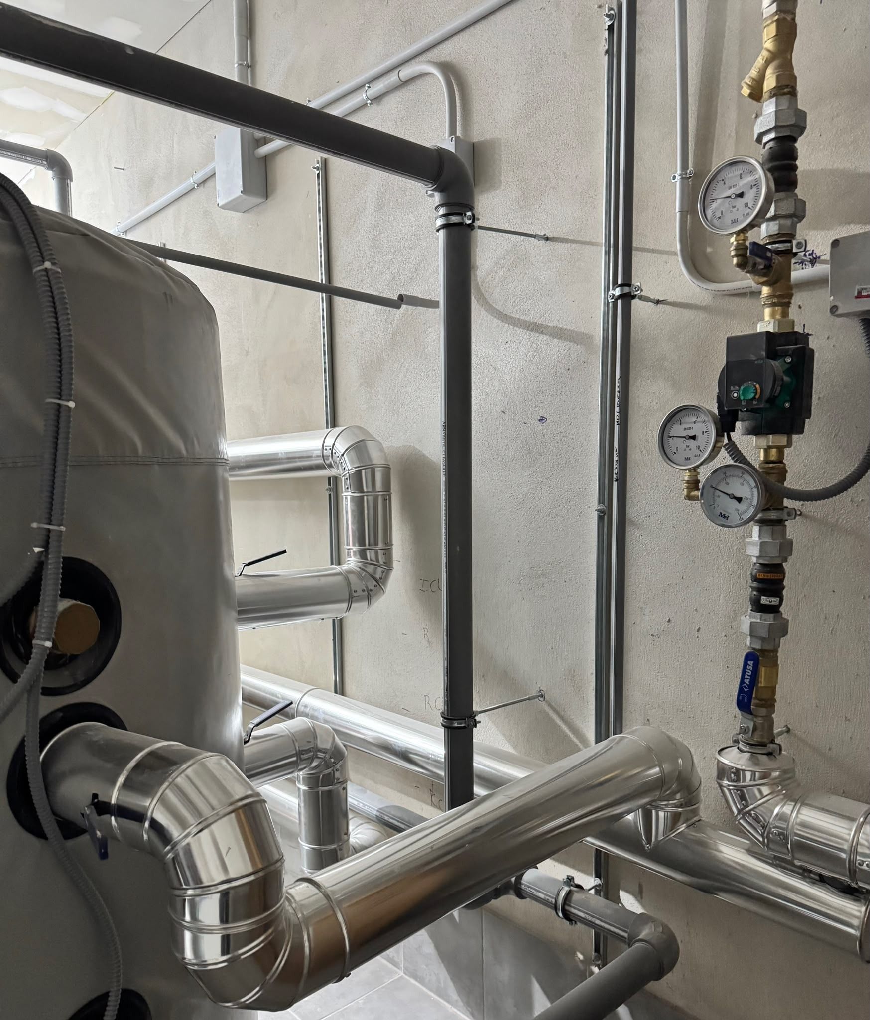 Tuberías industriales y manómetros en una pared de una sala de máquinas, con conductos aislados y relucientes