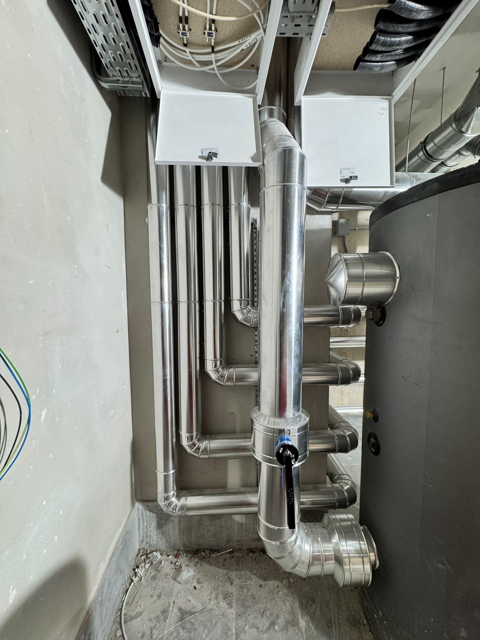 Cuarto de instalaciones industriales con tuberías plateadas a la vista, válvulas y cajas blancas montadas en la pared
